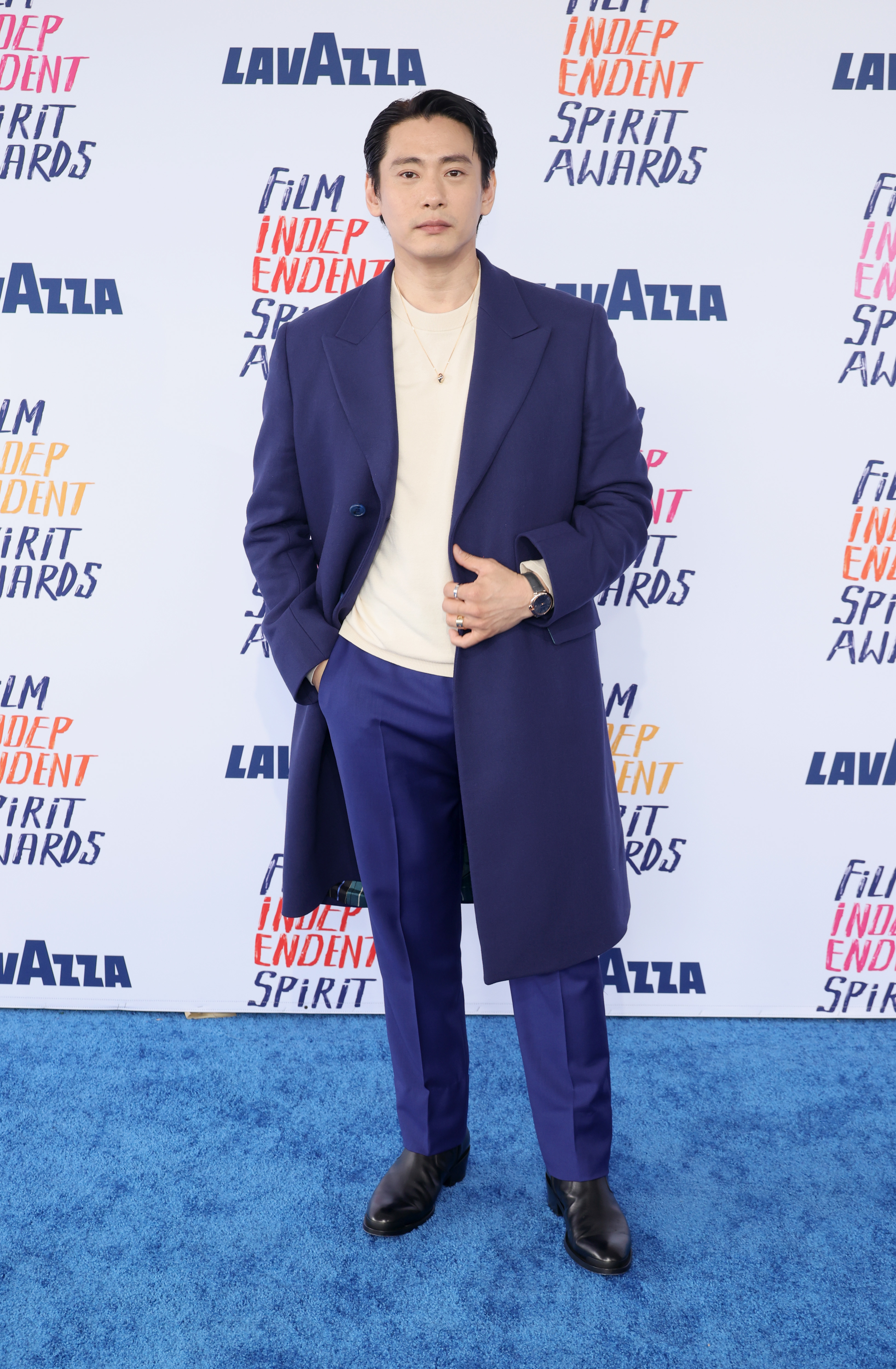 Teo Yoo in a coat over a top and trousers