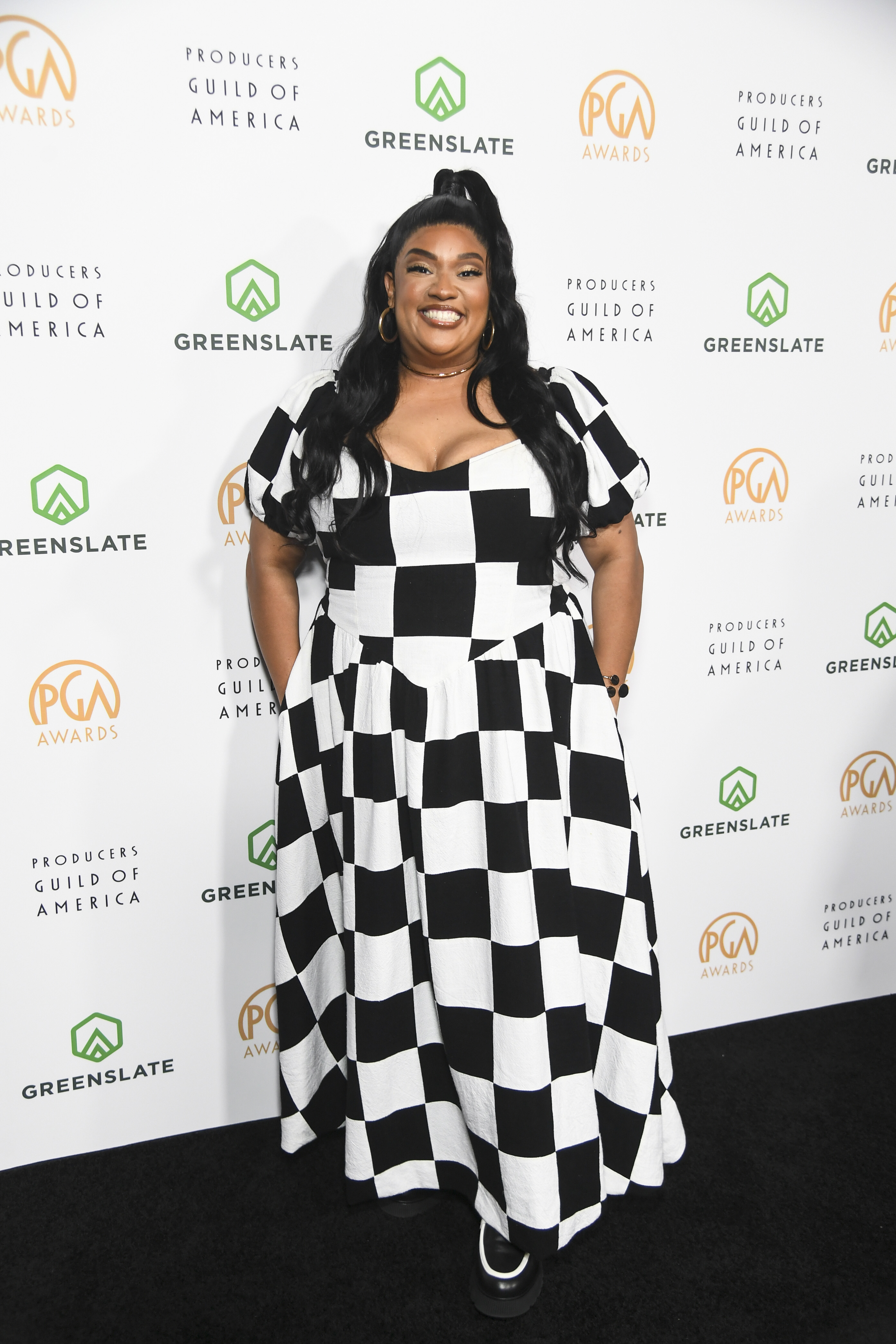 X Mayo in a checkered gown poses at the Producers Guild Awards