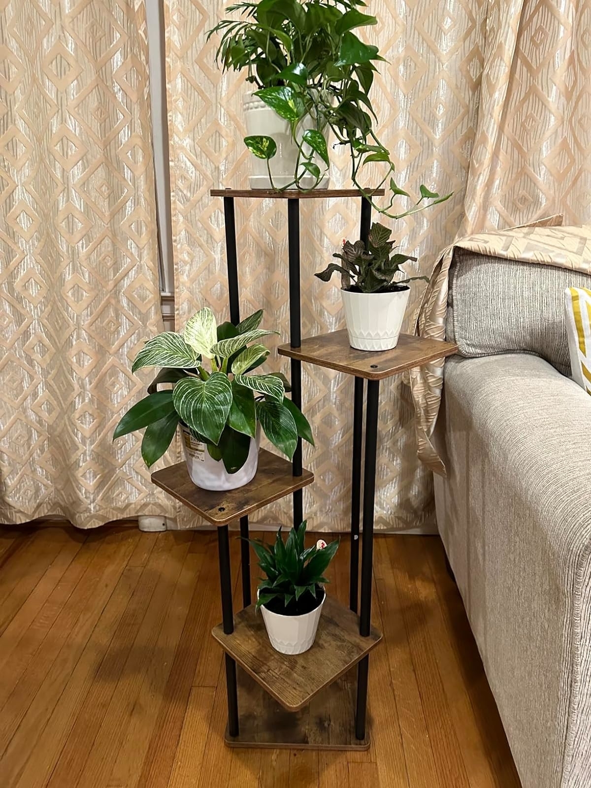 Three-tiered wooden and metal stand with various houseplants beside a sofa