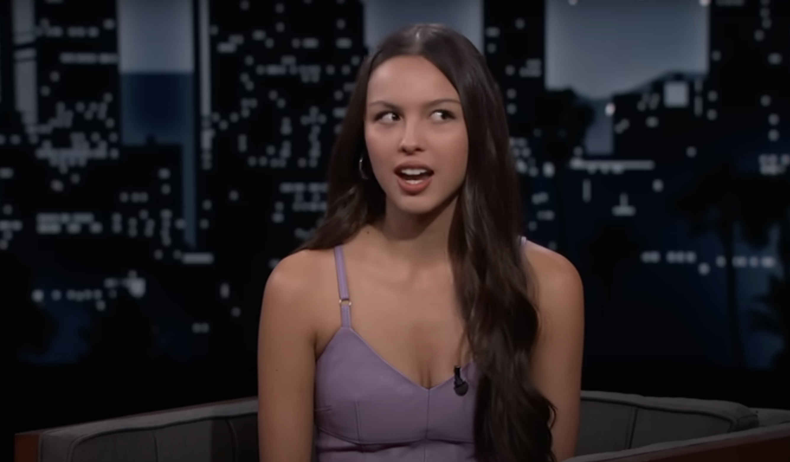 Olivia in a sleeveless dress speaking on a talk show