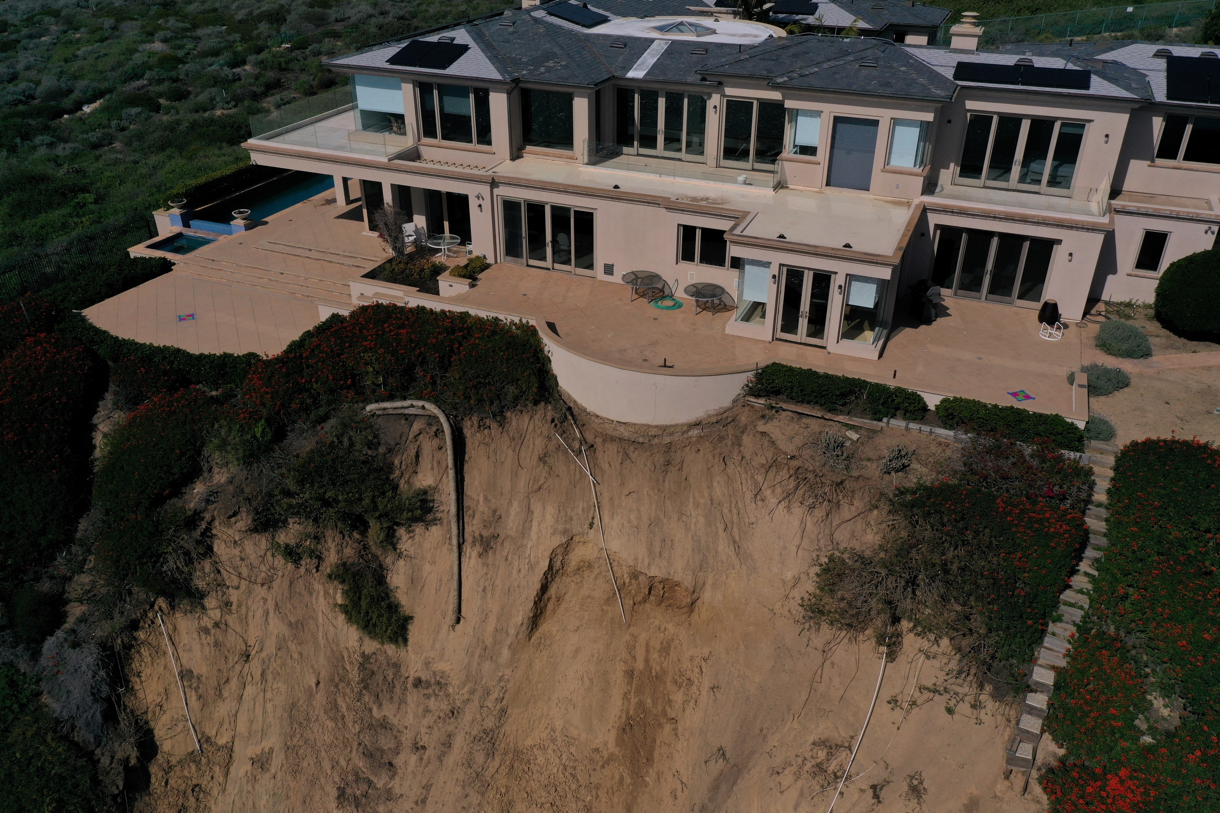 Aerial view of a large house perched on the edge of an eroded cliff
