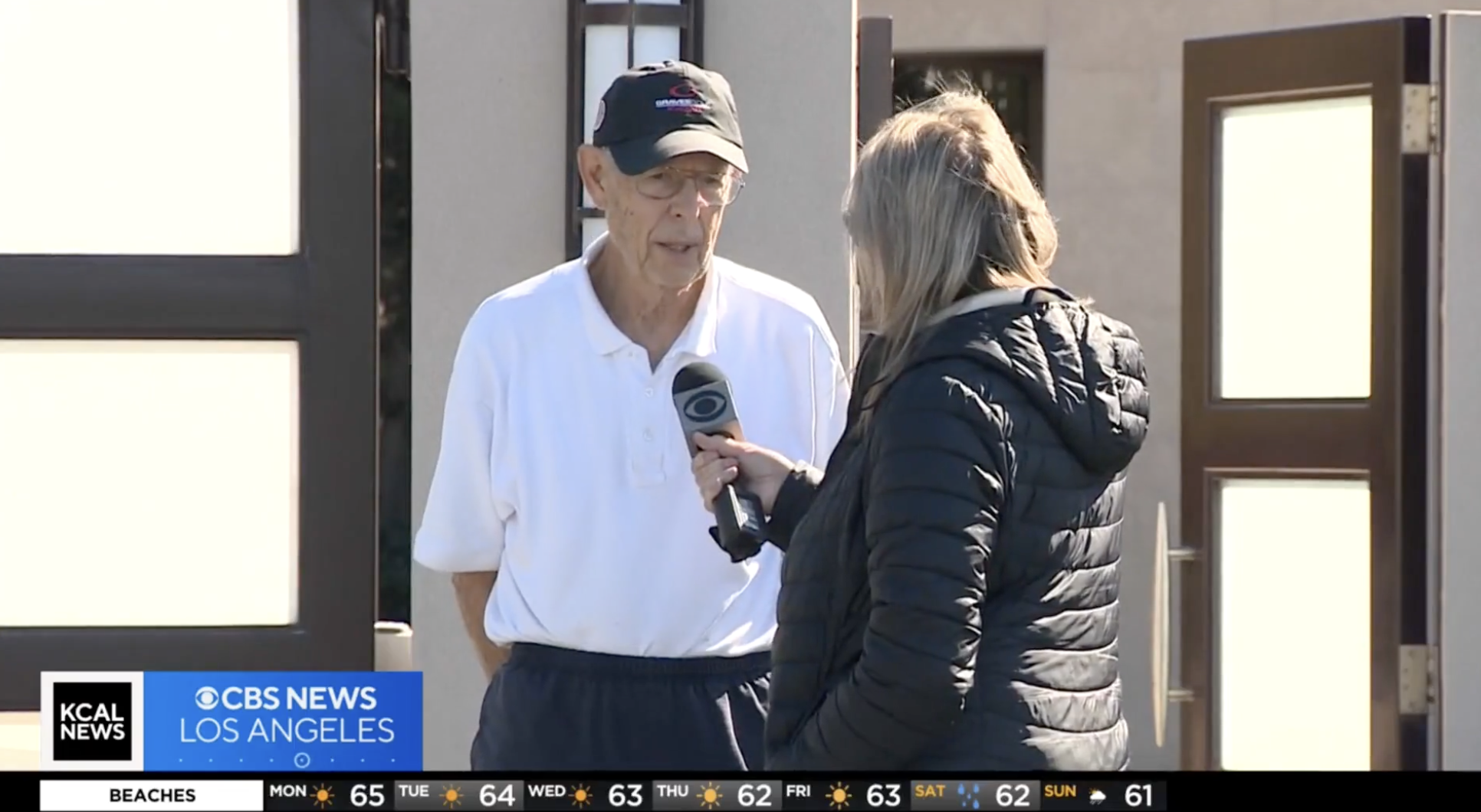 Elderly man being interviewed by a reporter outdoors, both holding a mic, with KCAL News logo on screen