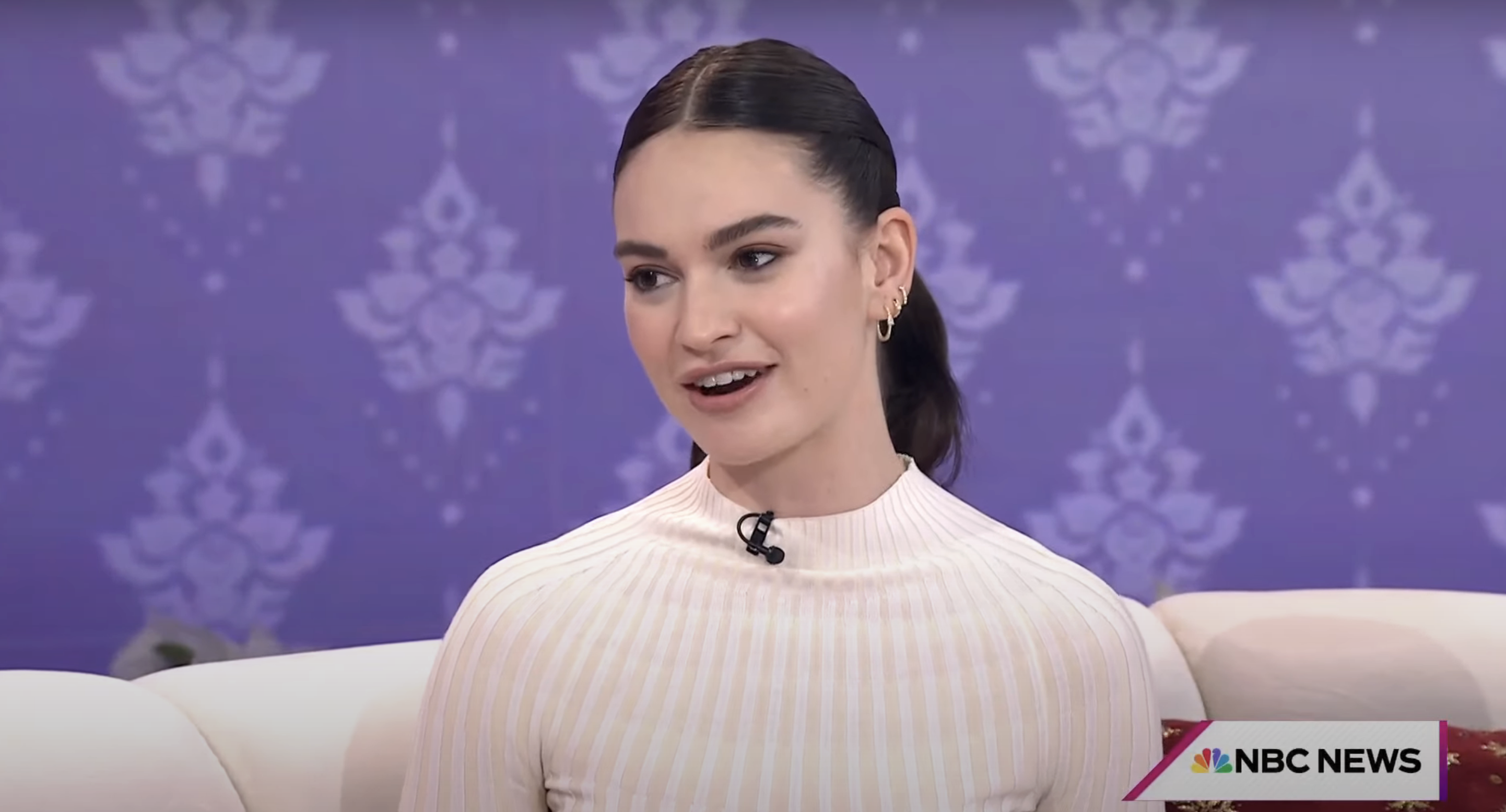 Lily in a ribbed top with a high collar, sitting on a sofa during a TV interview