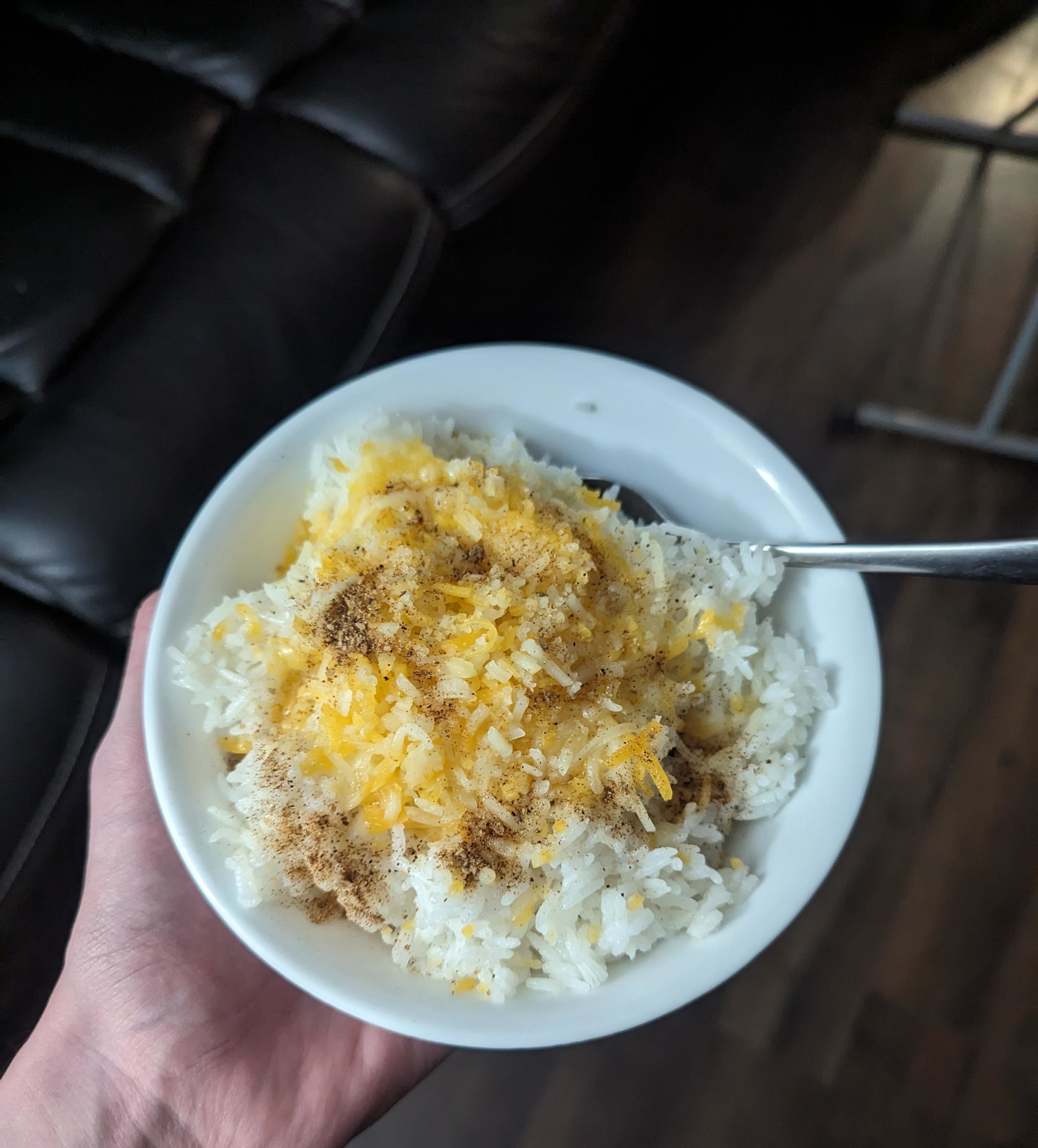 A person holding a bowl of rice topped with cheese and seasonings, viewed from above