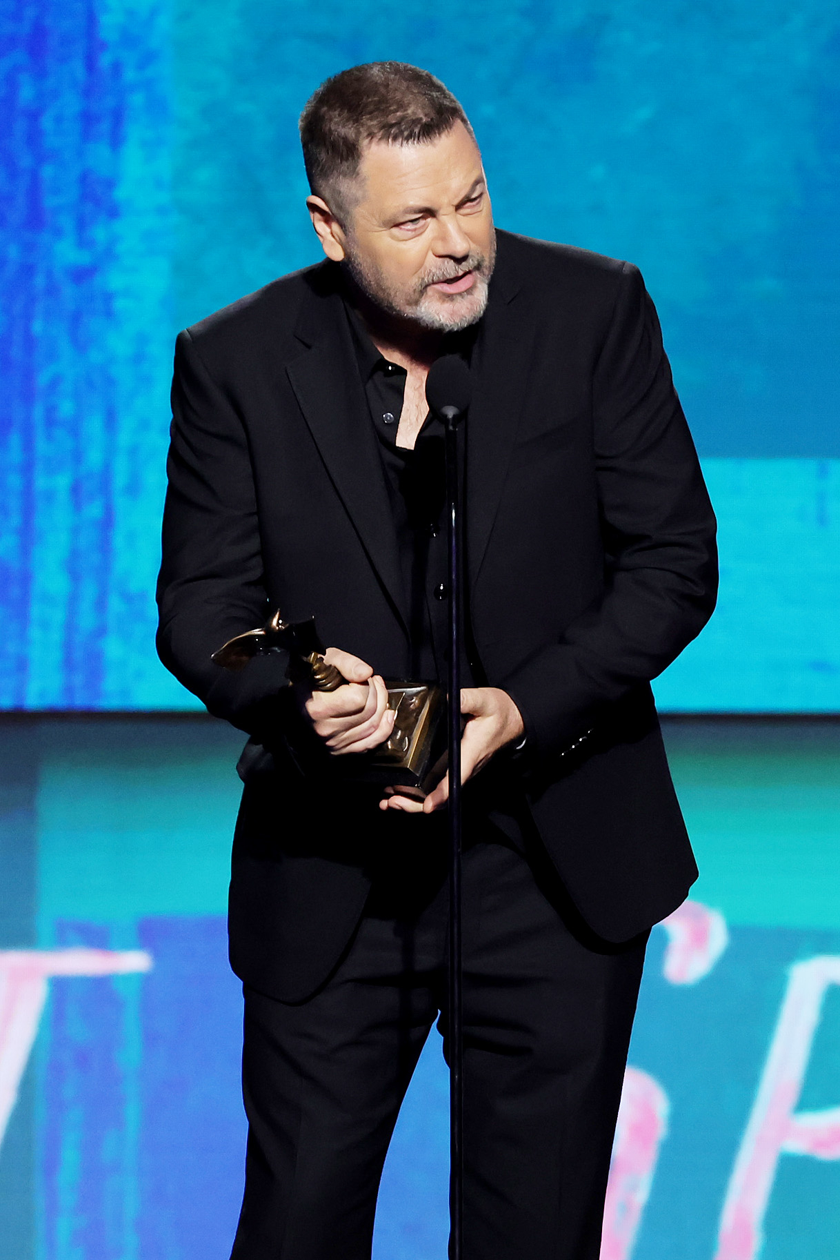 Nick Offerman in a suit holding his award onstage