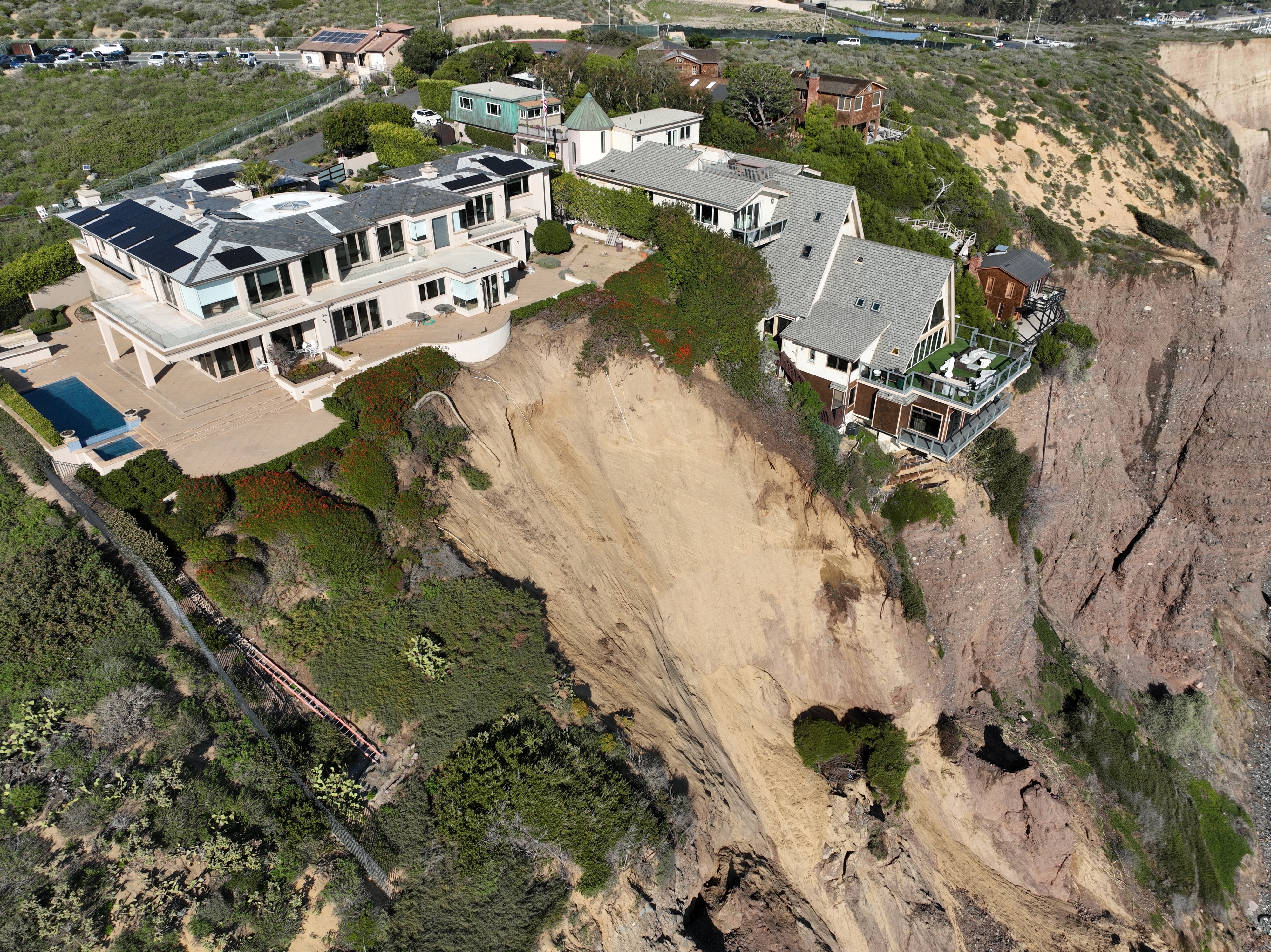 Aerial view of coastal homes on the edge of a cliff with visible erosion