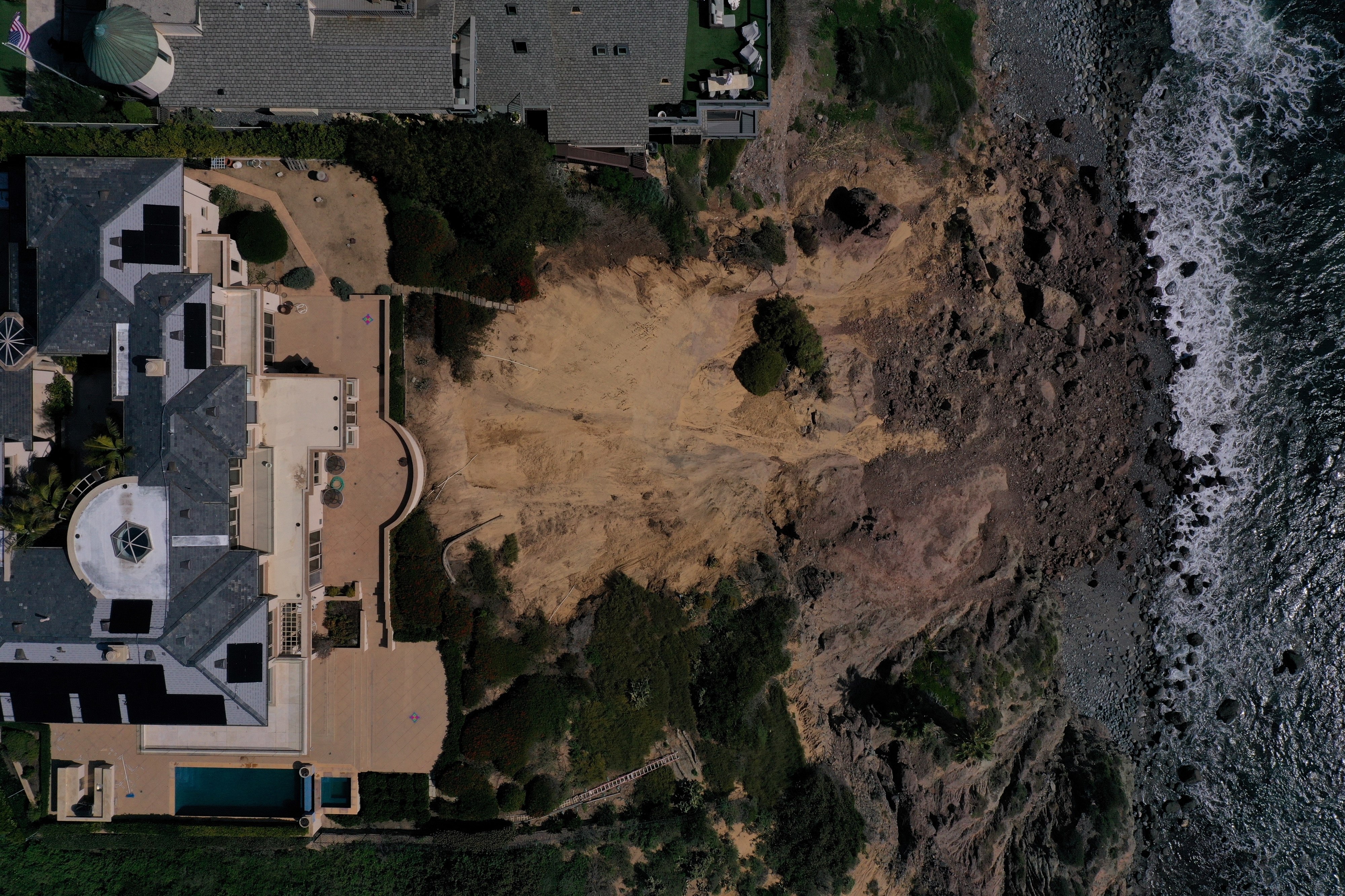 Aerial view of a coastal home next to a large landslide area