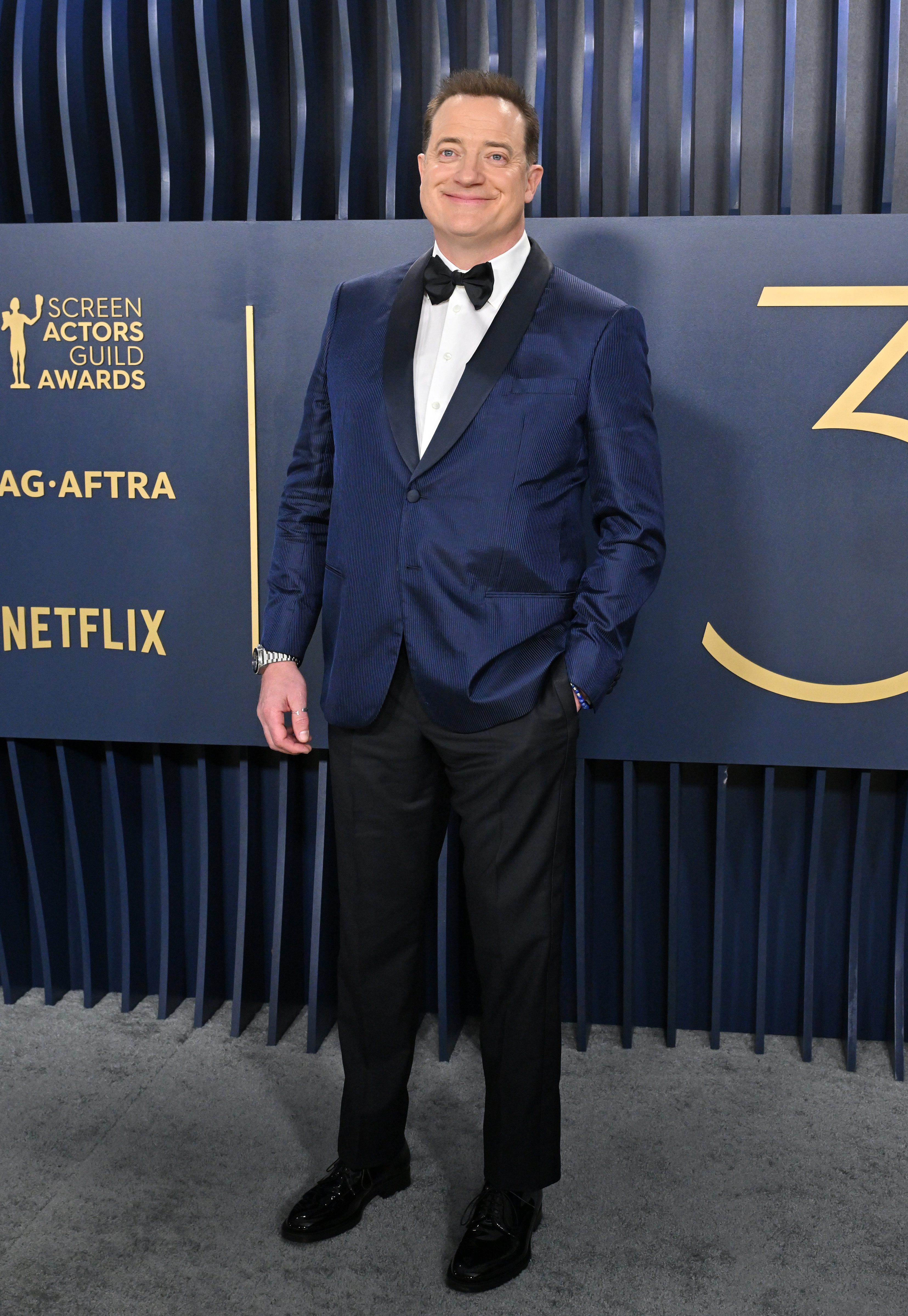 Brendan in a textured suit and bow tie standing against event backdrop