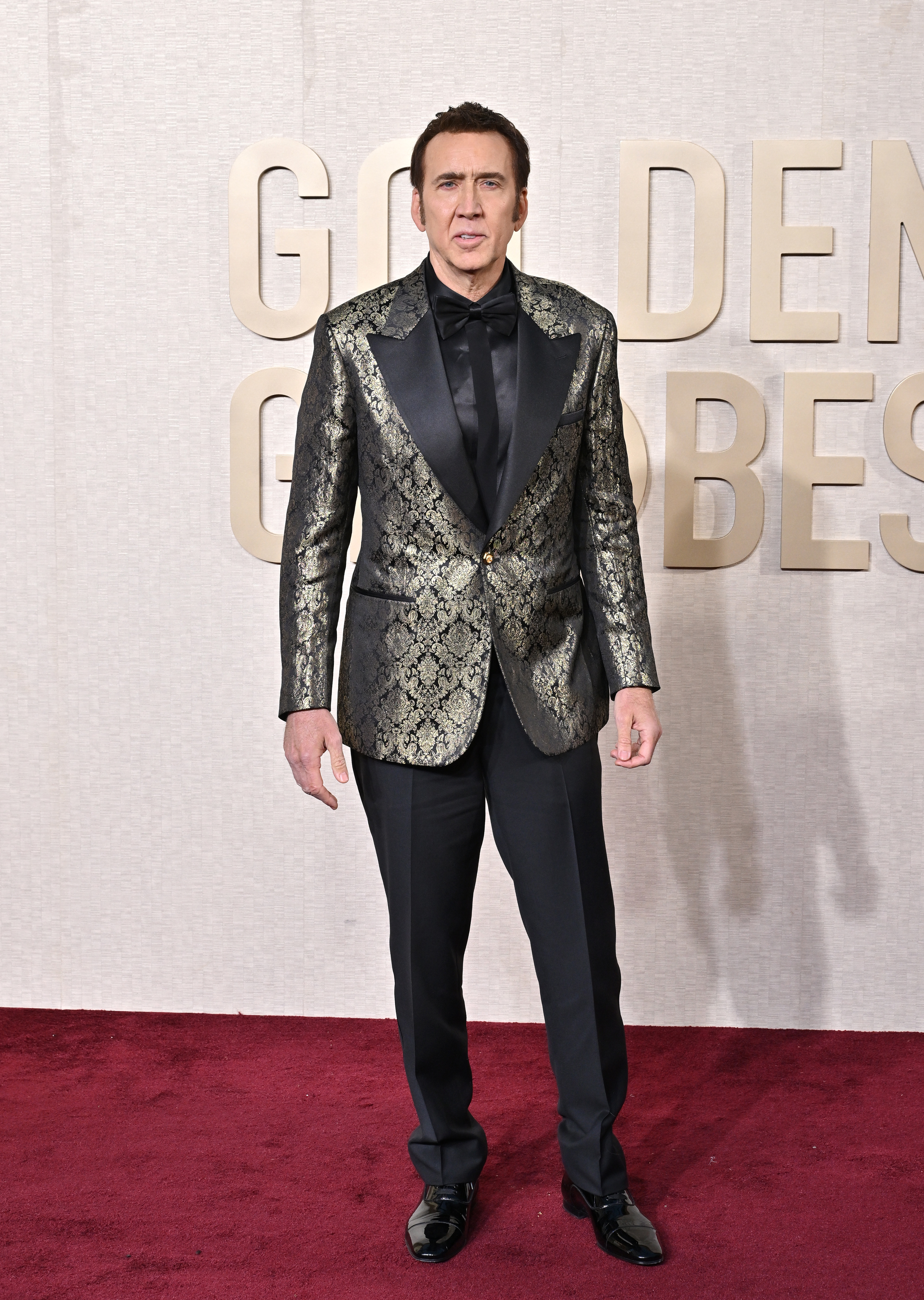 Nicholas Cage in patterned suit jacket and pants stands at a media event