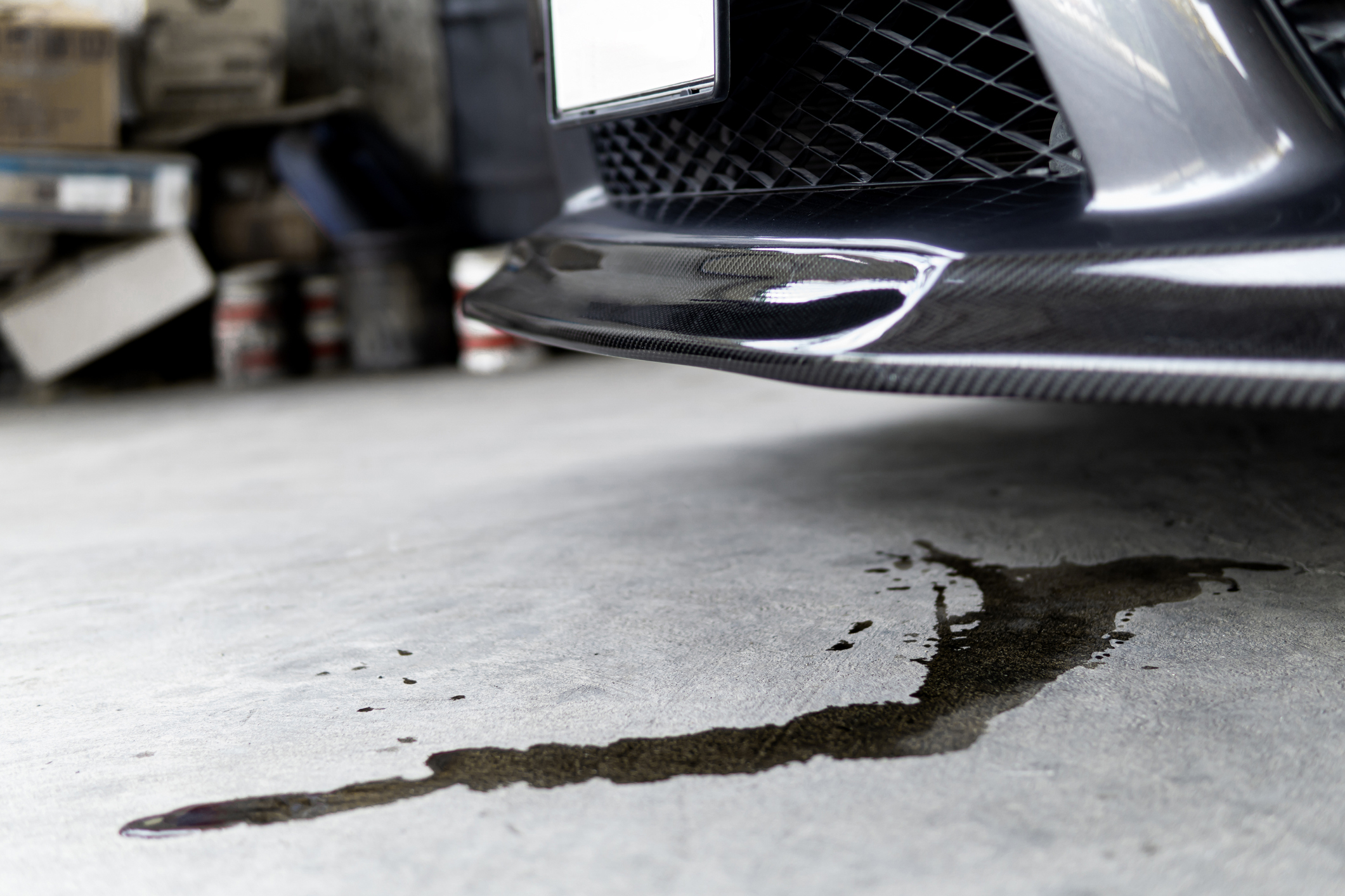 Close-up of a vehicle&#x27;s front with oil leaking onto a concrete floor