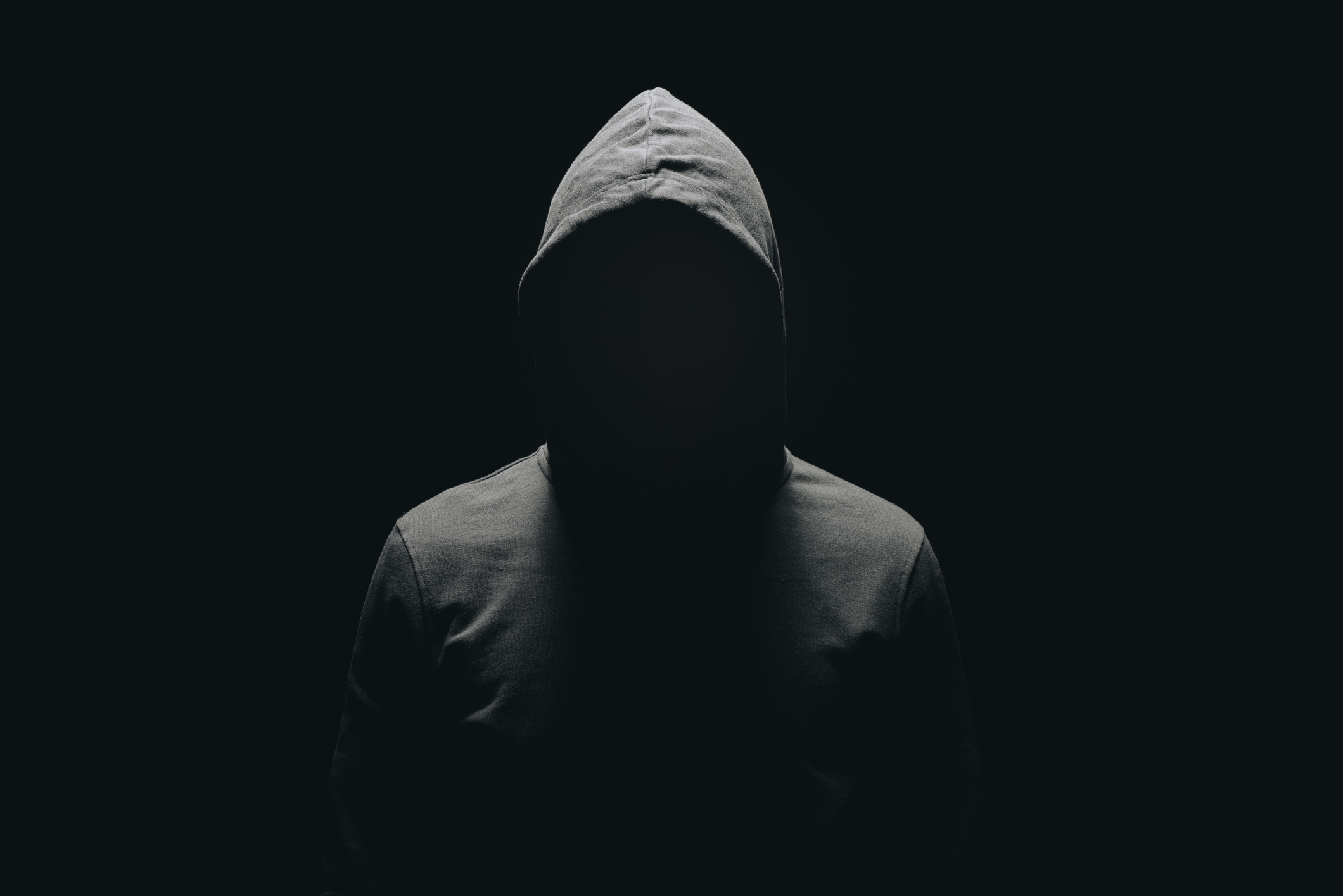Silhouette of an unidentified person in a hooded top against a dark background, posing anonymously