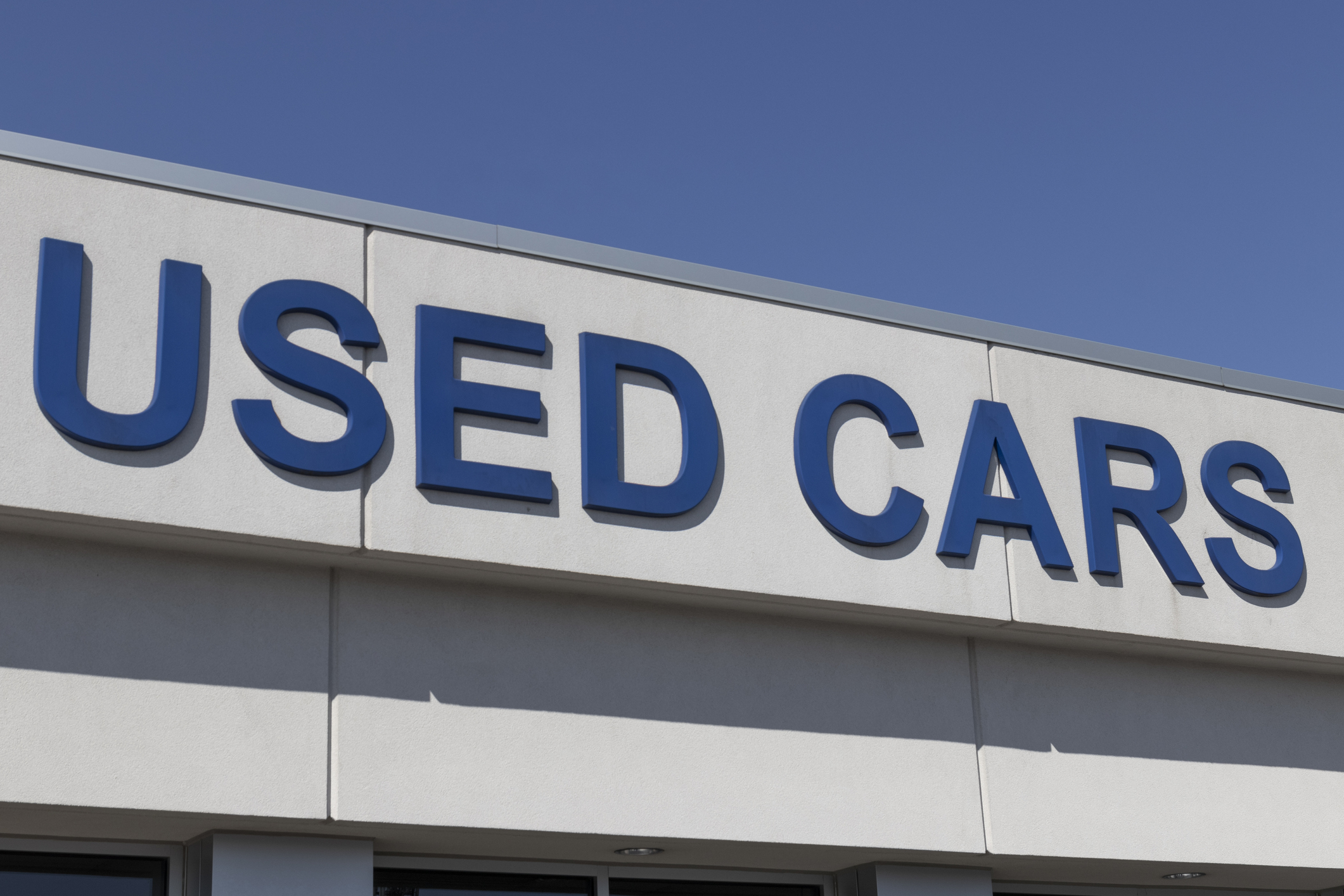 Sign with text &quot;USED CARS&quot; on the facade of a building against a clear sky
