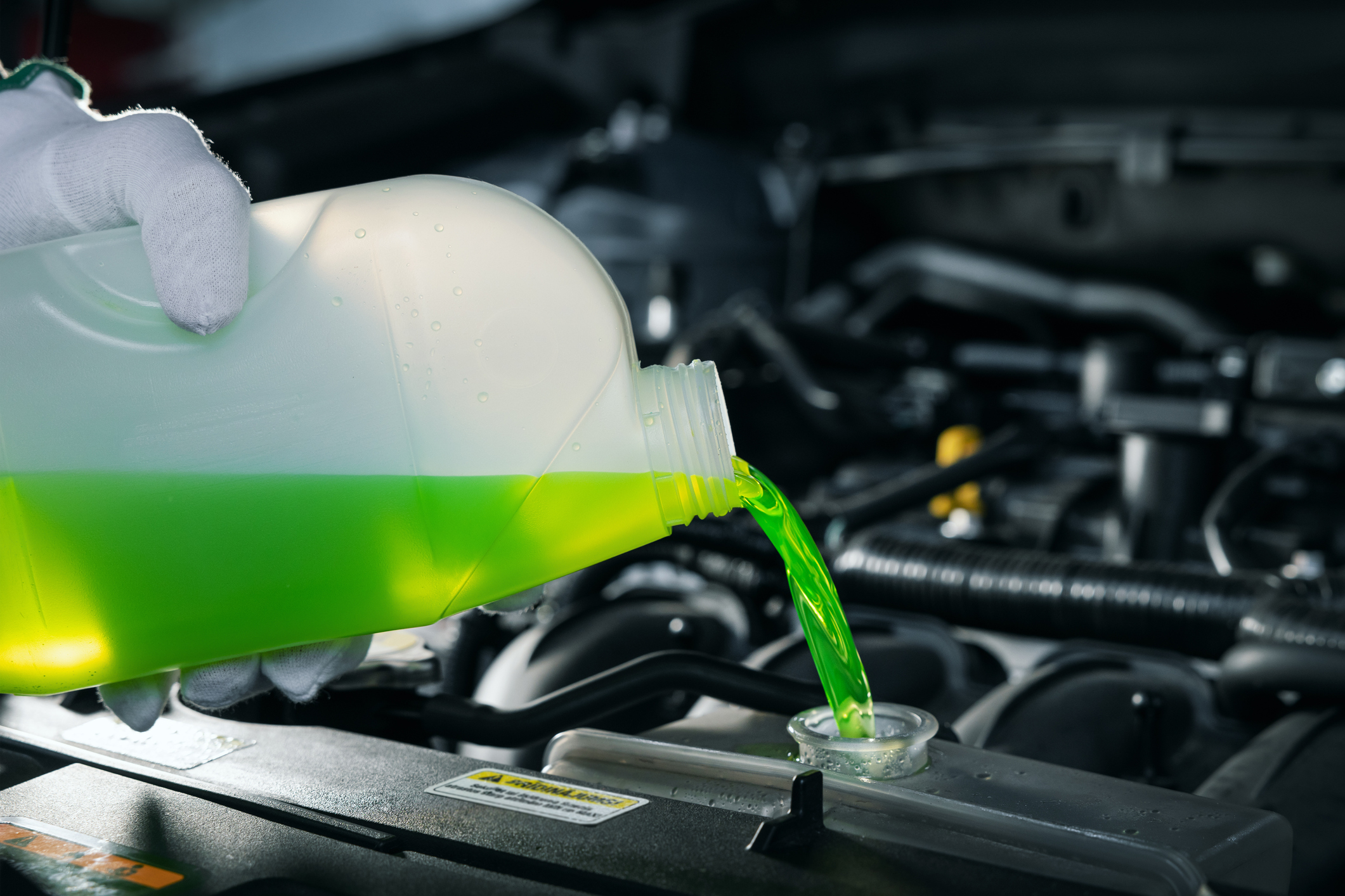 Pouring green coolant into a car engine from a plastic jug, with engine details visible