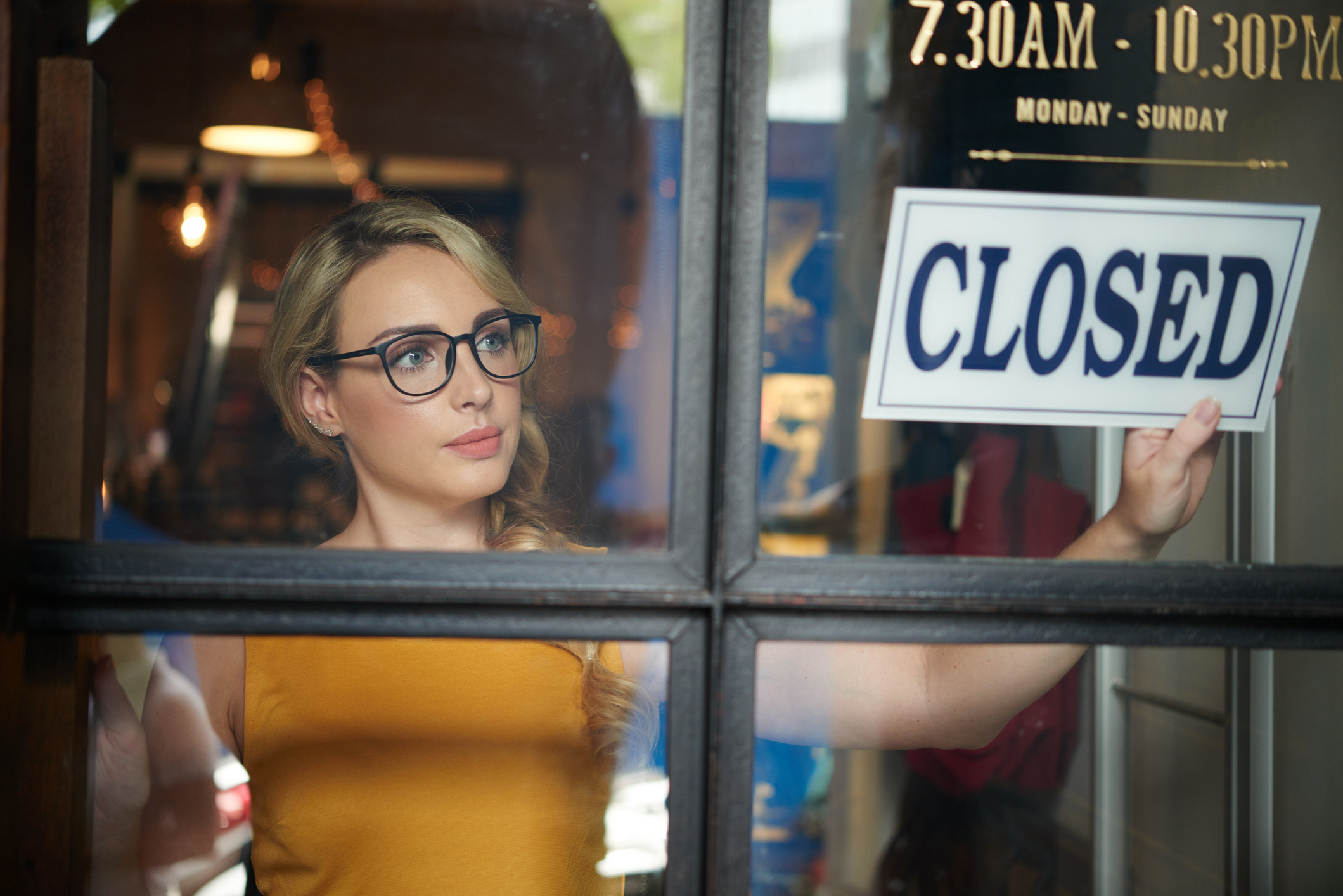 Woman holding a &#x27;CLOSED&#x27; sign inside a door, looking outward