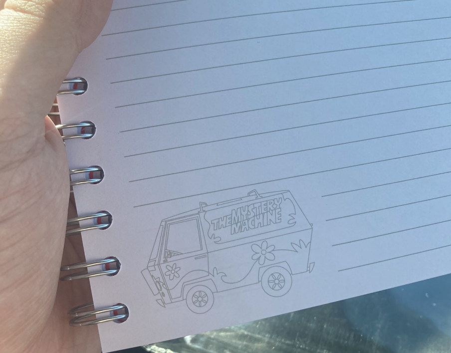 Hand holding an open notebook with a drawn image of the Mystery Machine from Scooby-Doo on its lined pages