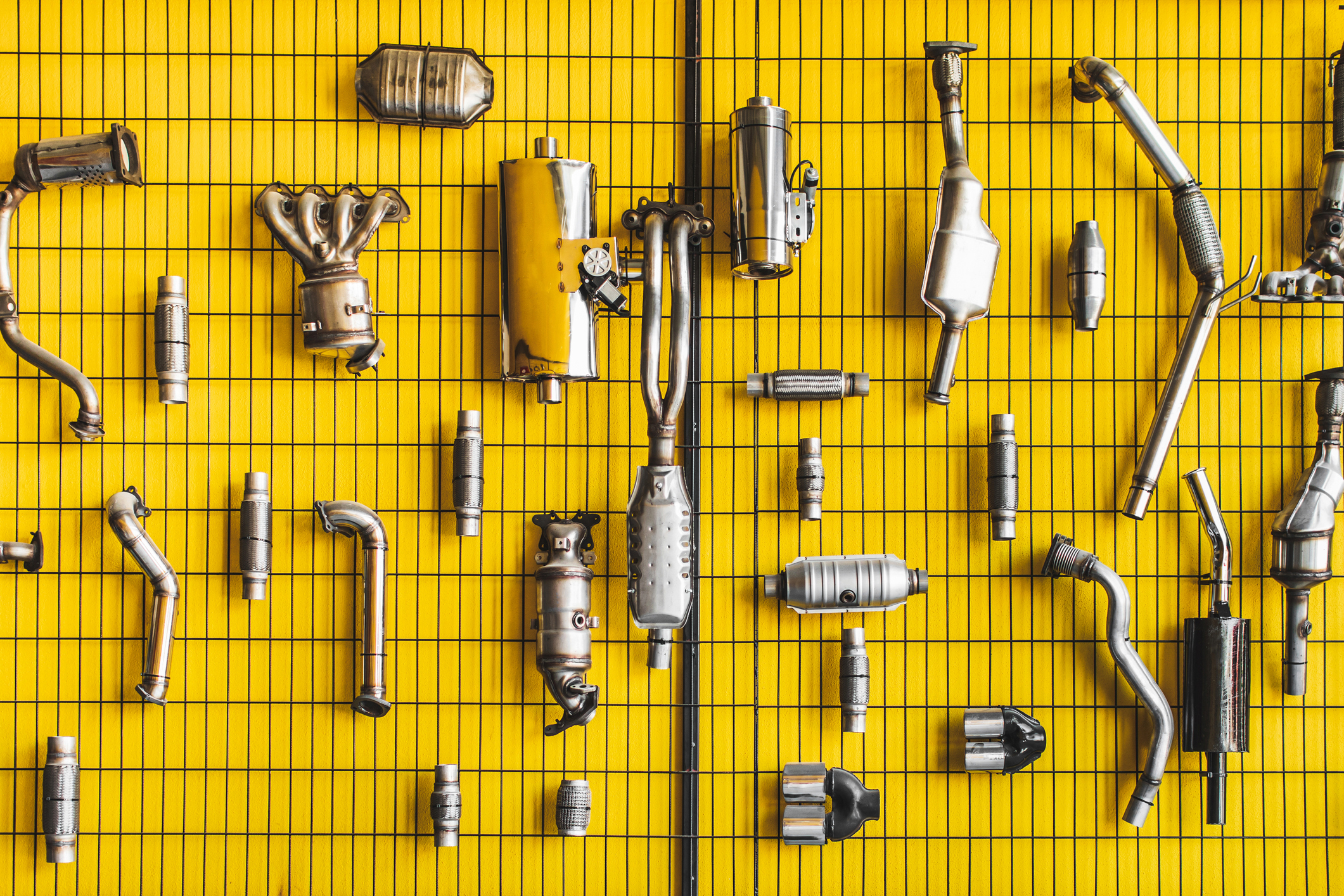 Assorted car exhaust parts displayed in an organized fashion on a yellow grid wall