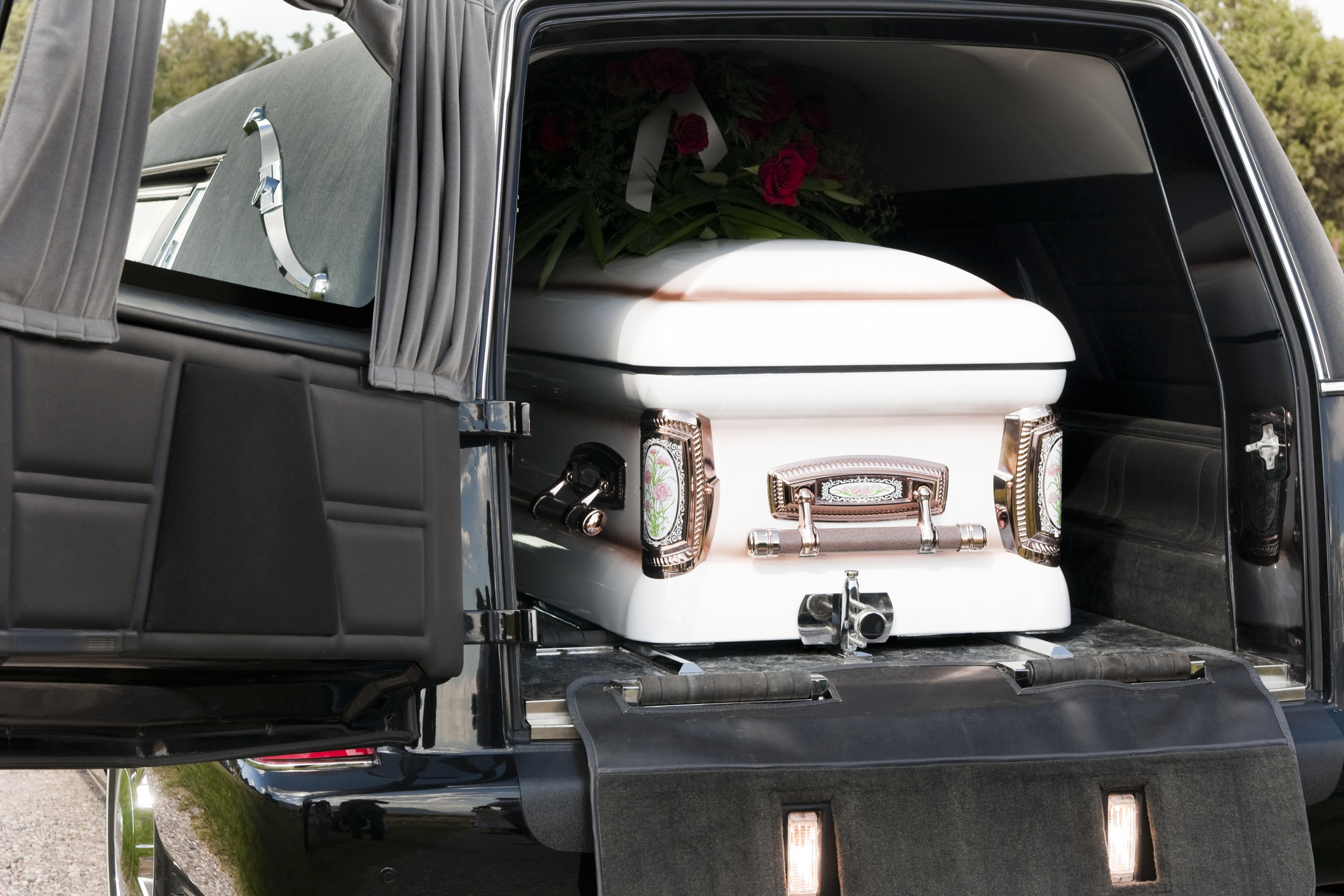A hearse with its rear door open, displaying a white casket adorned with flowers inside