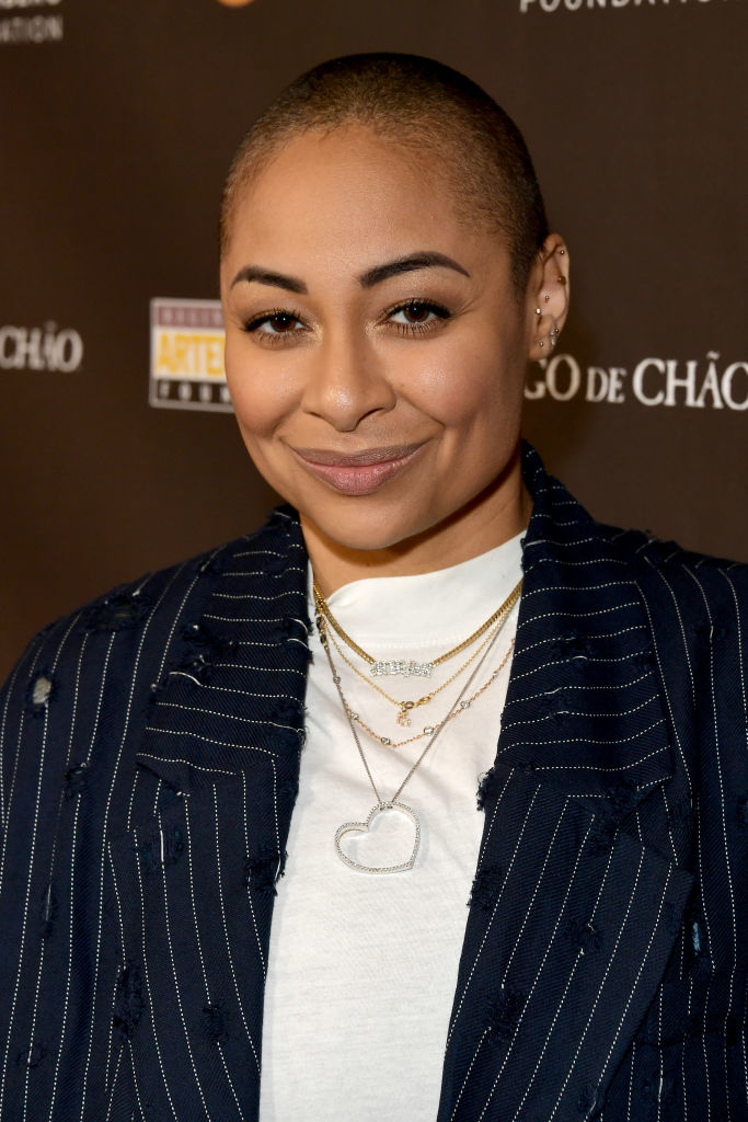 Raven-Symoné posing, wearing a pinstripe suit with necklaces, with a buzzed head