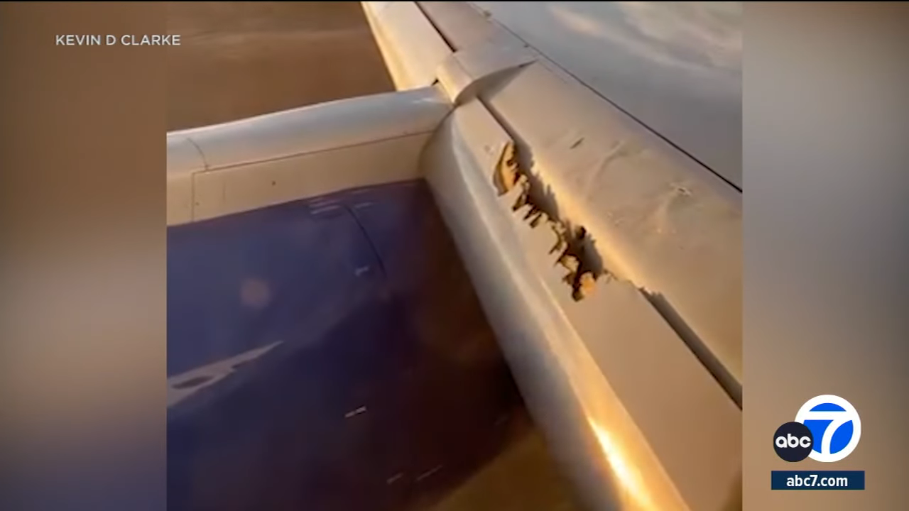 Airliner wing with visible damage and torn metal, viewed from inside the plane through a window