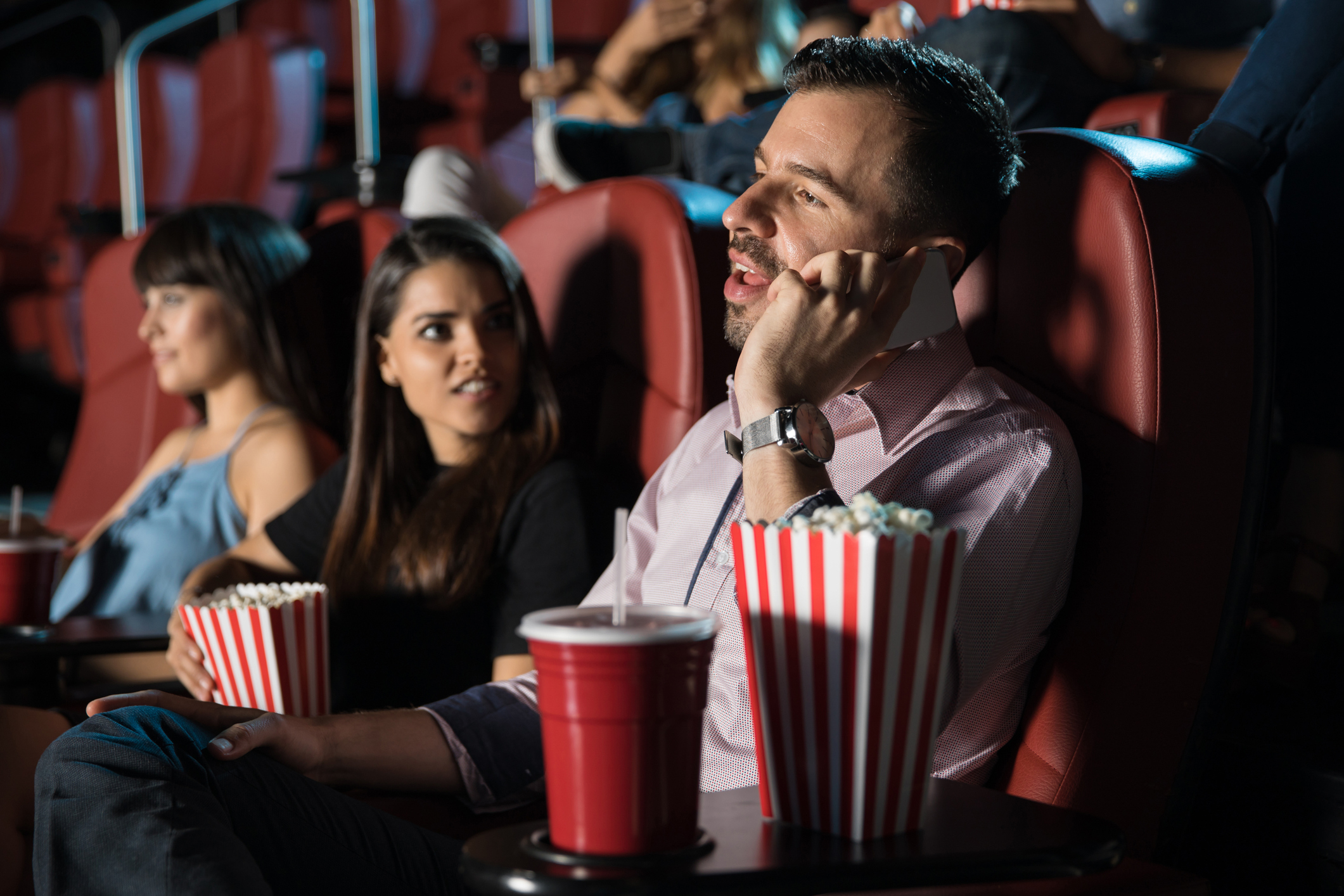 Man talking on phone in a cinema, disturbing others; woman next to him looks annoyed