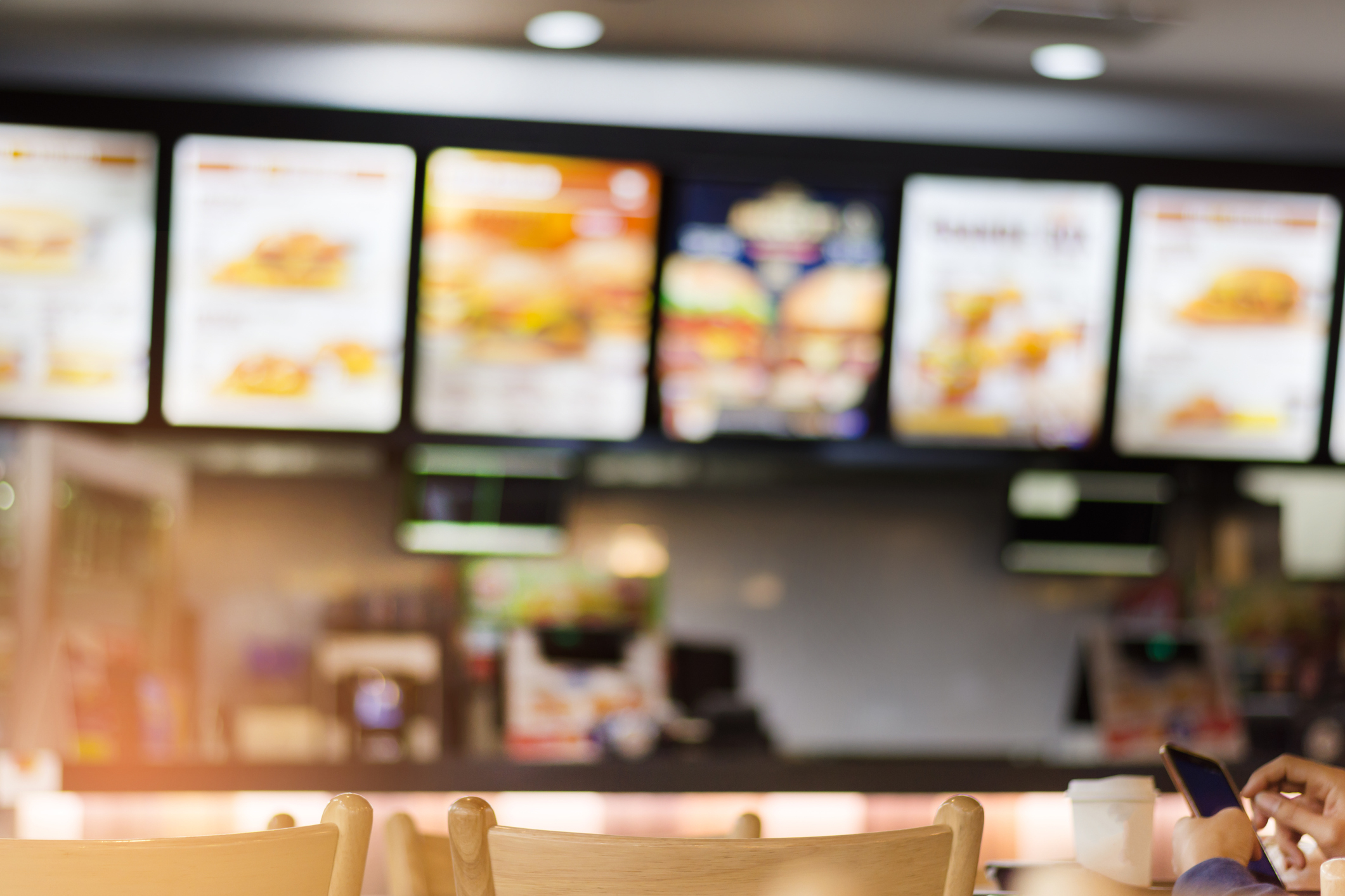 Fast food restaurant menu boards above counters, blurred with foreground seating