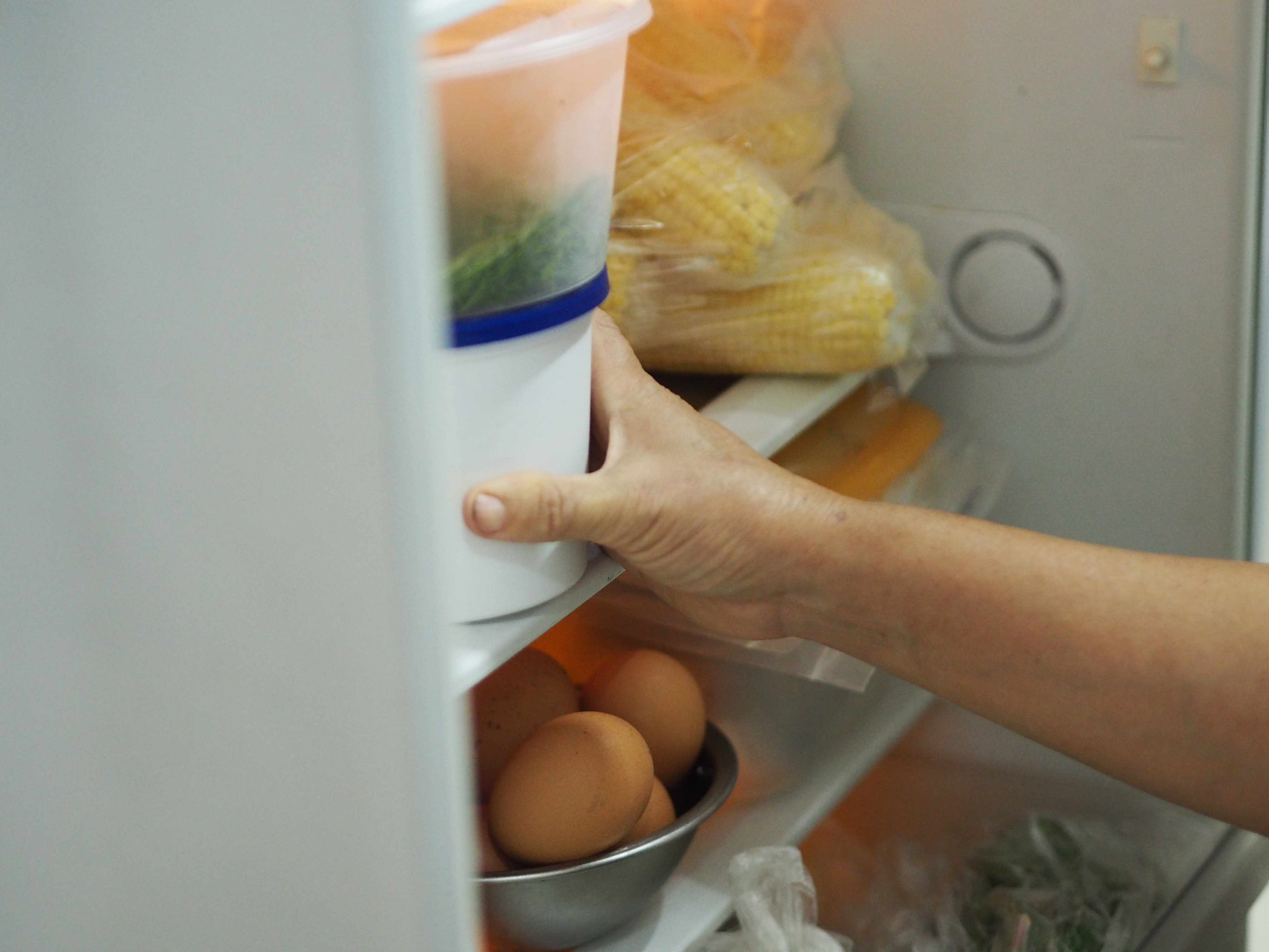 Person&#x27;s hand opening a refrigerator stocked with eggs and vegetables, implying budget-friendly meal planning