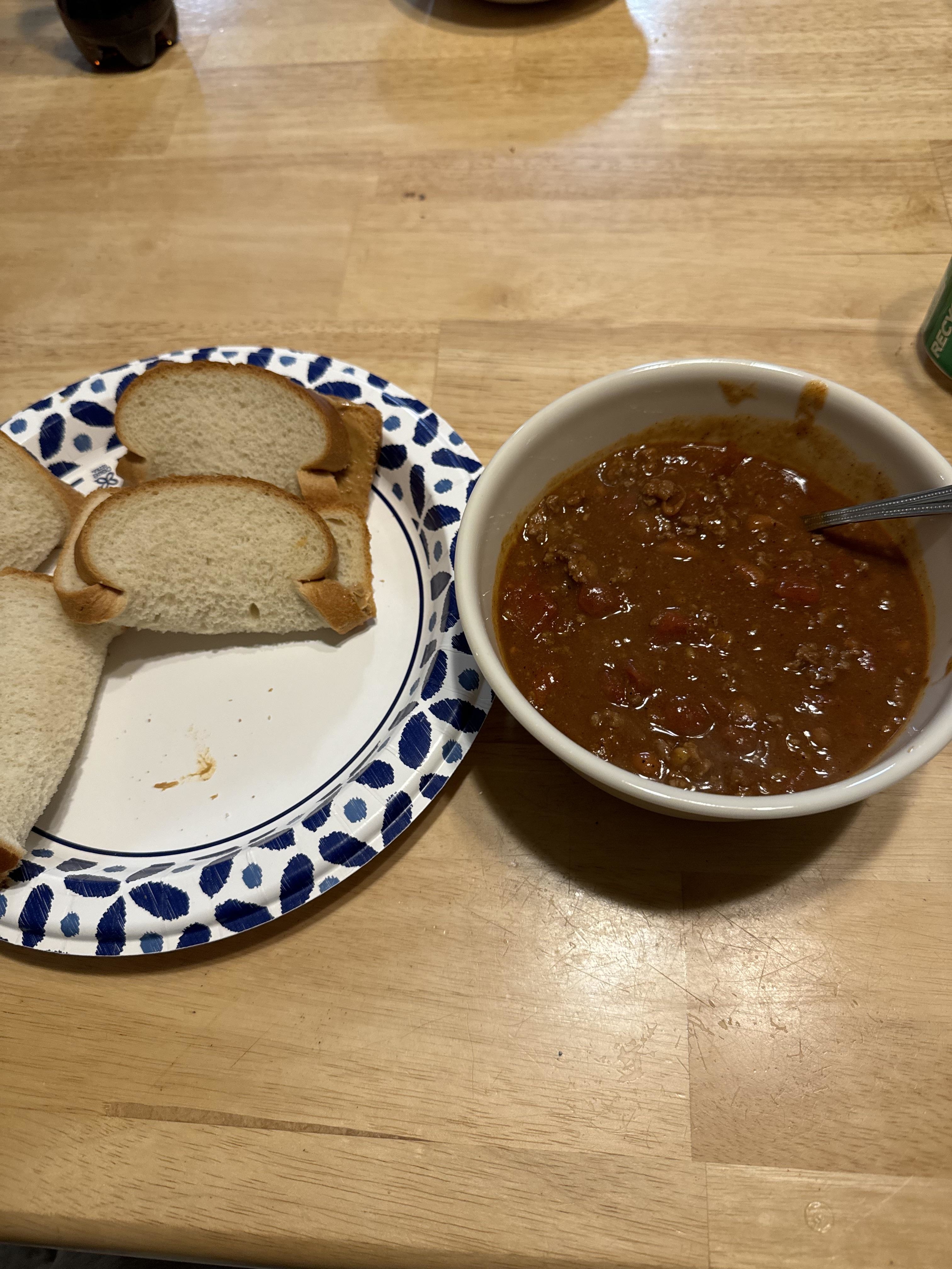 A bowl of chili next to a plate with two slices of bread with peanut butter