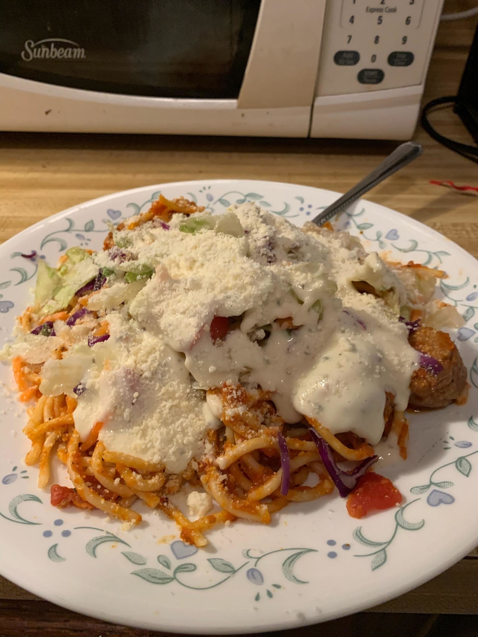 A plate of spaghetti with ranch topped with shredded cheese