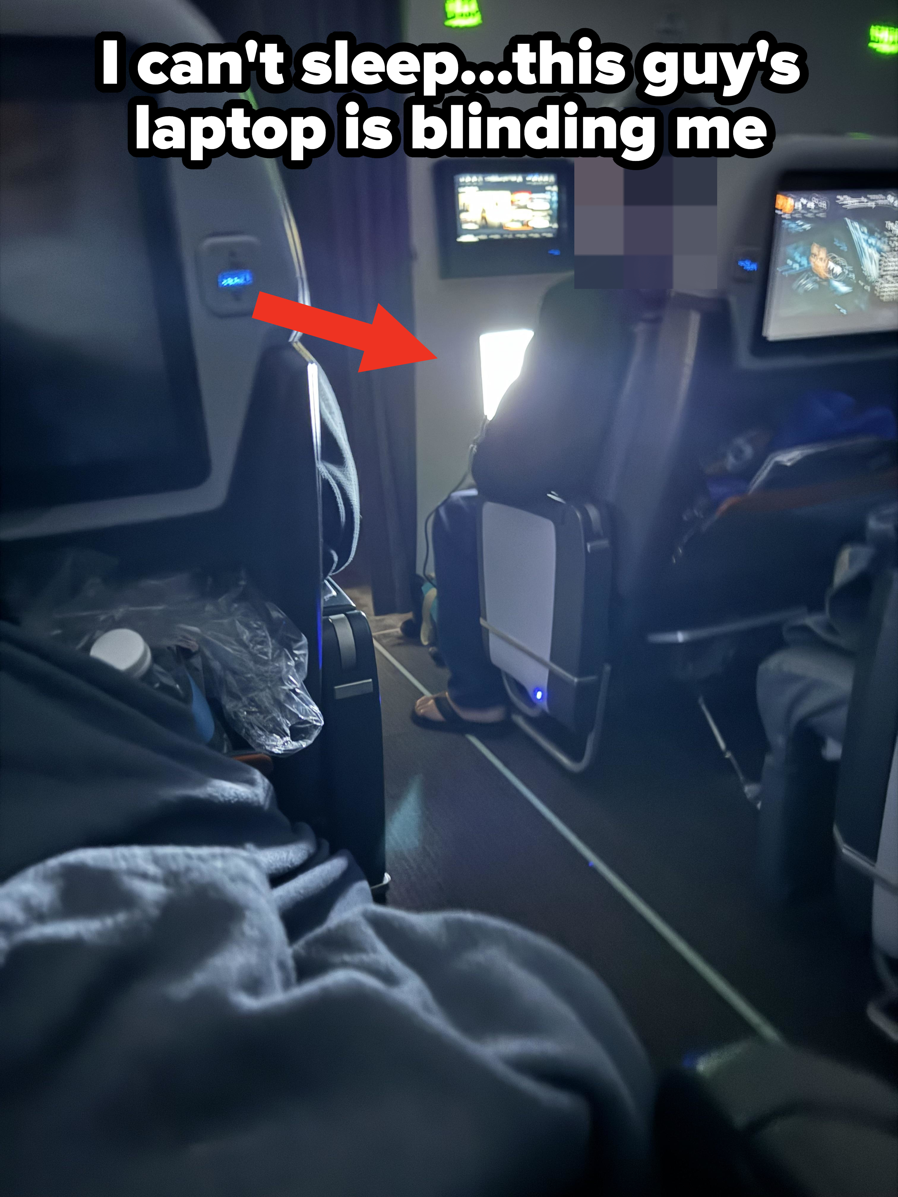 Passenger in an airplane seat in a dimly lit airplane with another very bright screen visible ahead with movie playing