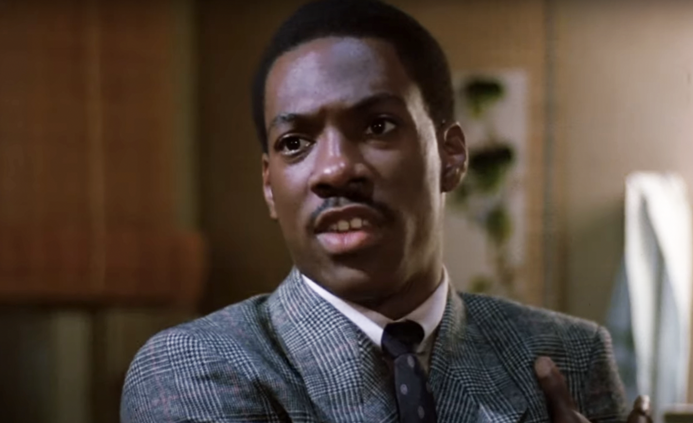 Eddie Murphy in character wearing a checkered jacket and tie