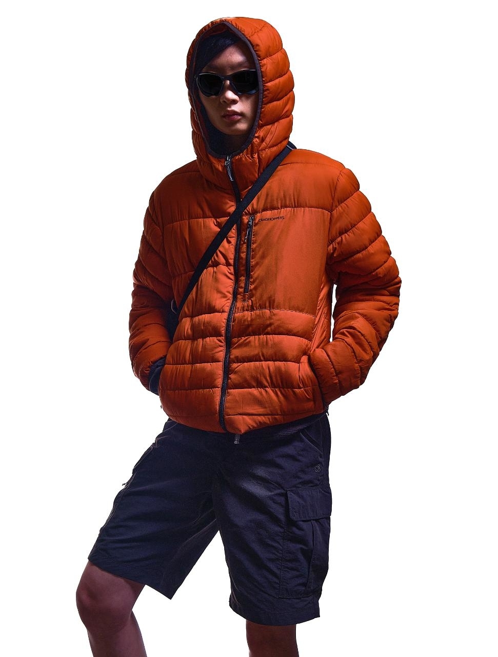 Individual in oversized puffer jacket with hood up, sunglasses, and shorts, hands in pockets, posing against a white background
