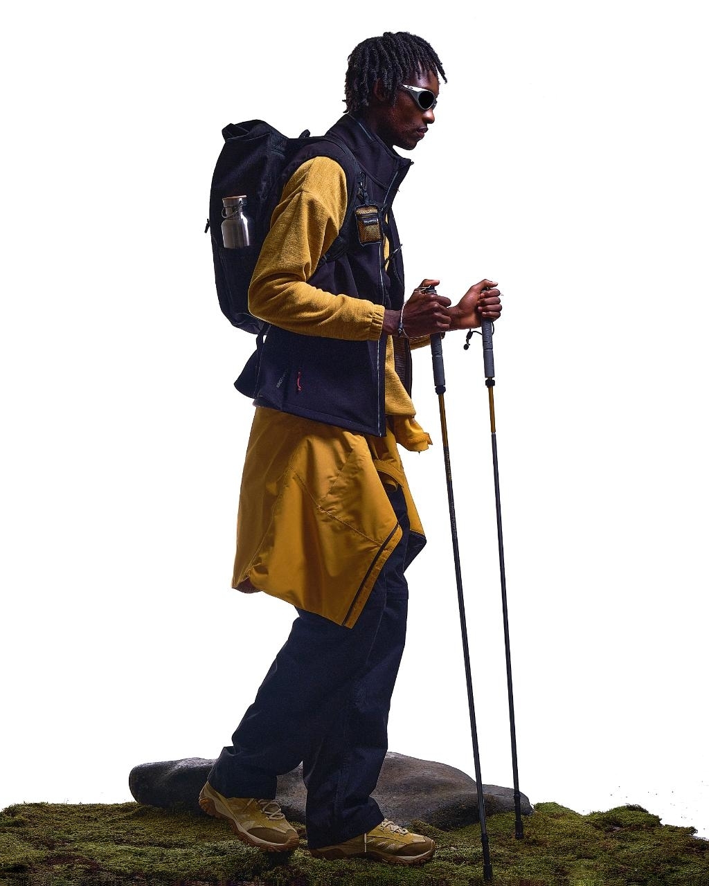 Man with backpack and walking poles in hiking attire, including a jacket and cargo pants