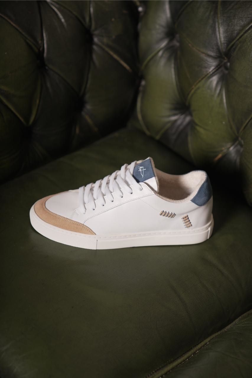 A single white sneaker with logo, placed on a green leather couch