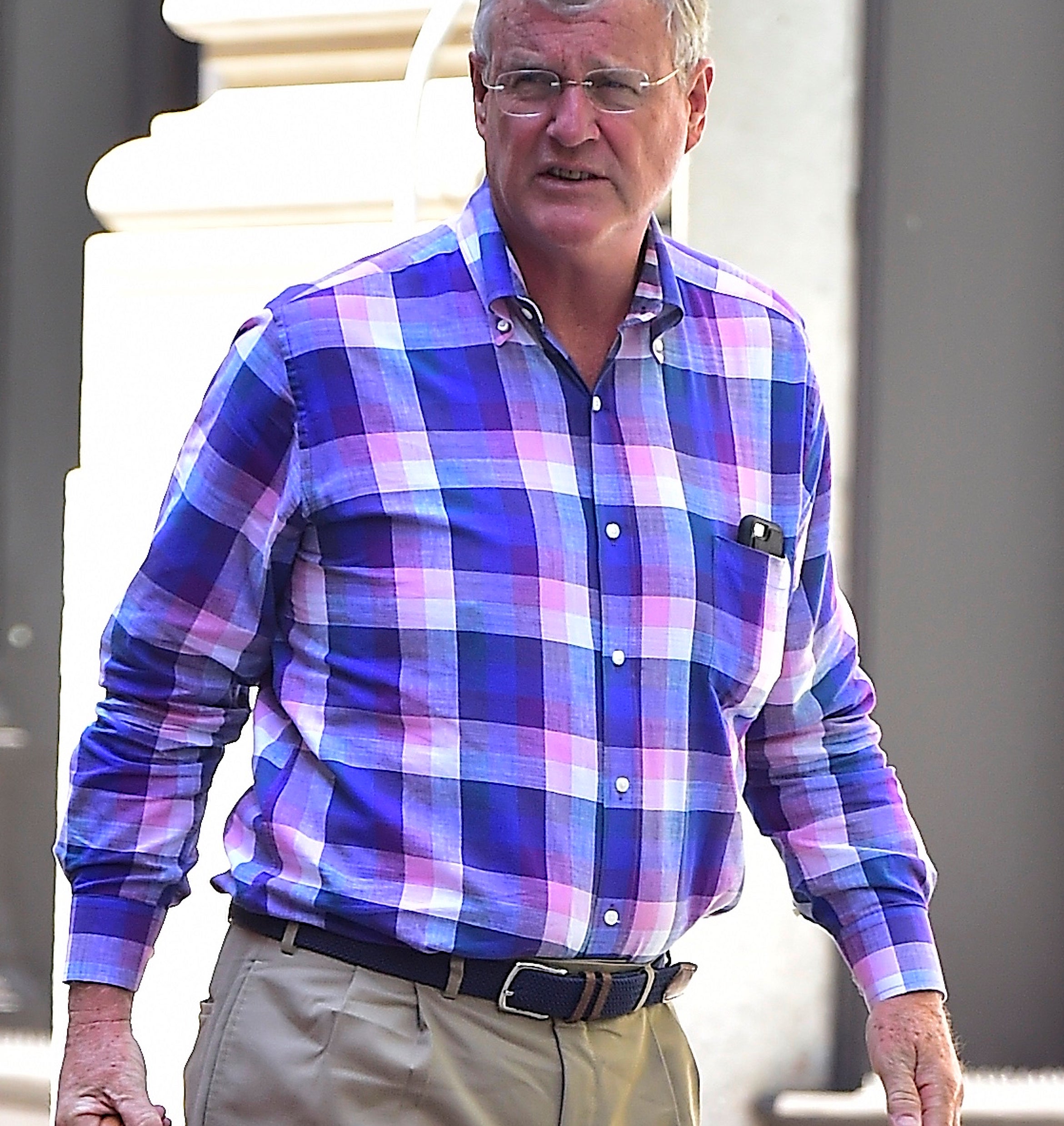 Scott Swift in a plaid shirt and khakis walking with a red bag