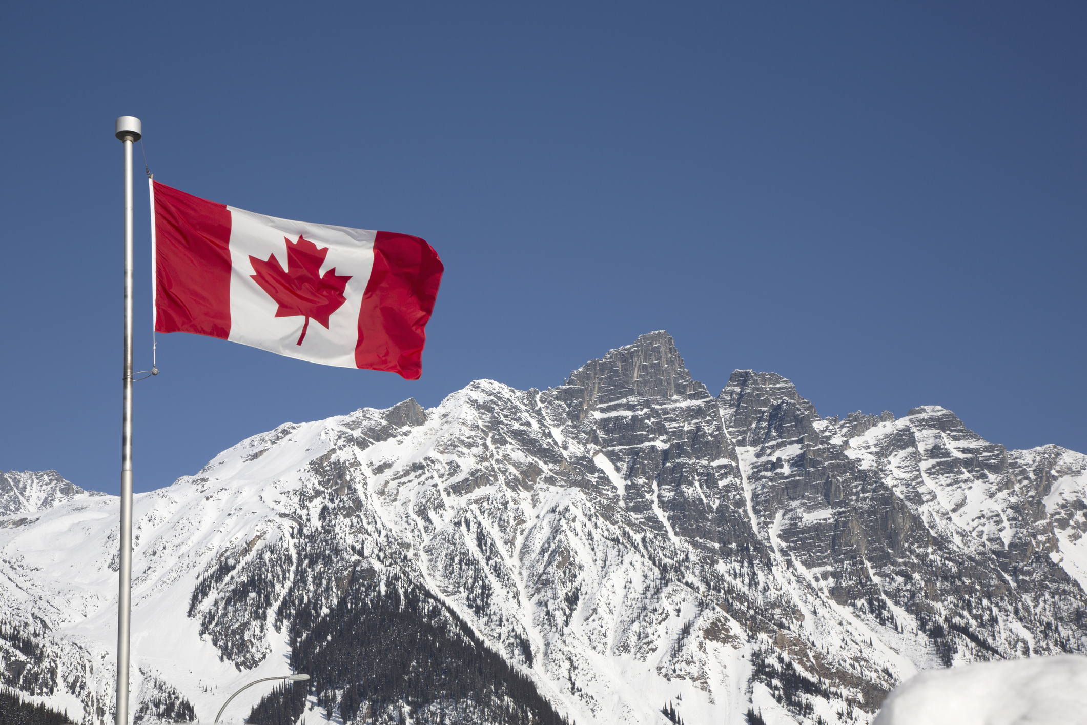 Canadian flag waving in front of snow-covered mountains