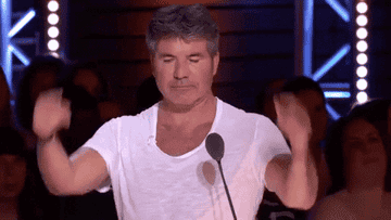 Man dancing with arms up in a casual white t-shirt on a talent show stage
