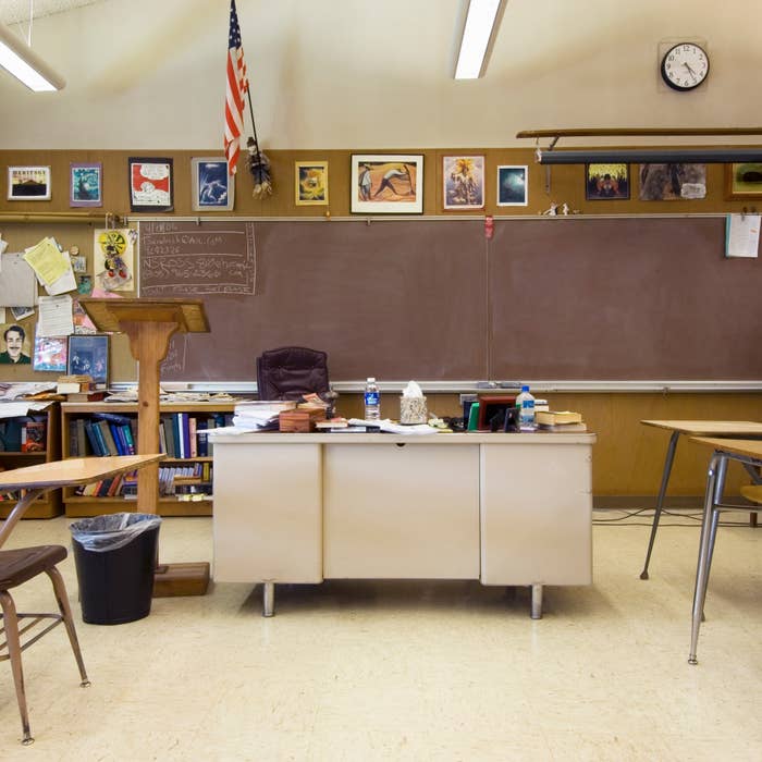 Empty classroom with teacher&#x27;s desk, student desks, American flag, and clock showing 10:10