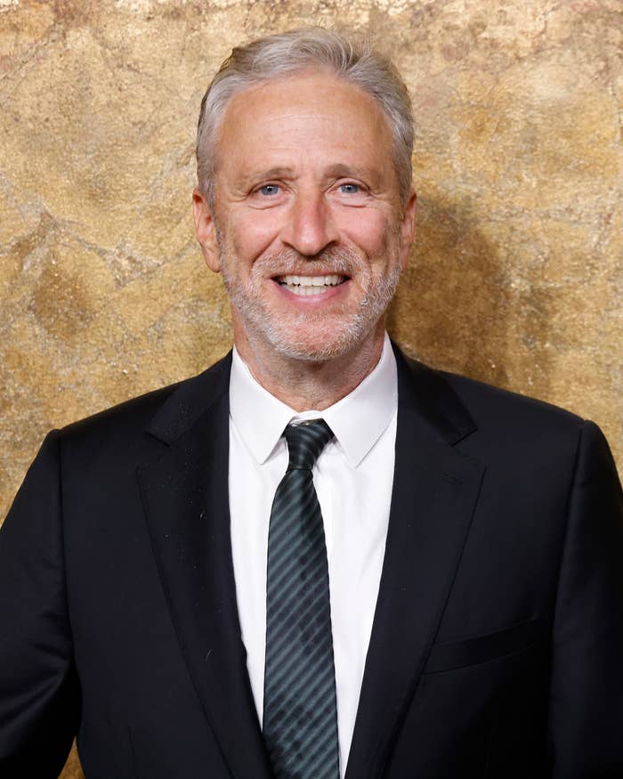 Jon Stewart smiling in a suit and striped tie