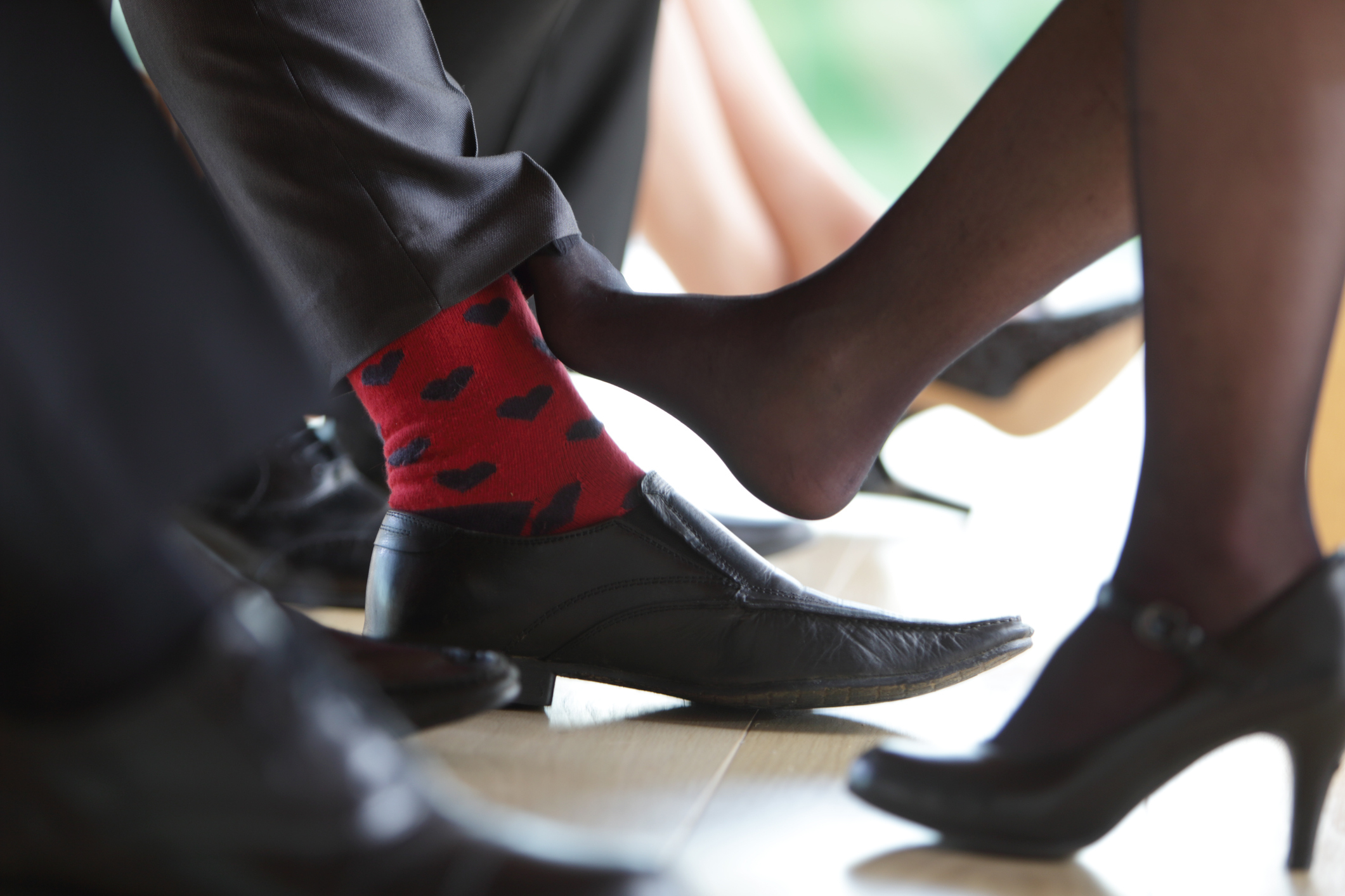 Close-up of two people flirting with their legs, one wearing whimsical heart-patterned socks