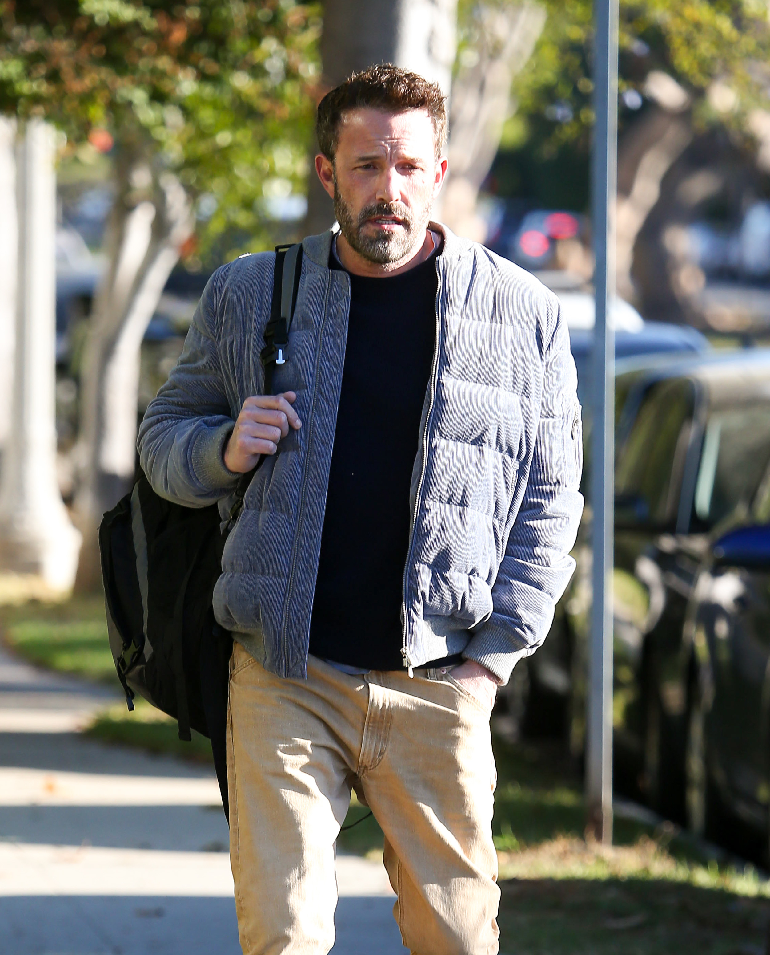 Ben in a casual attire with a jacket and backpack walking on a sidewalk