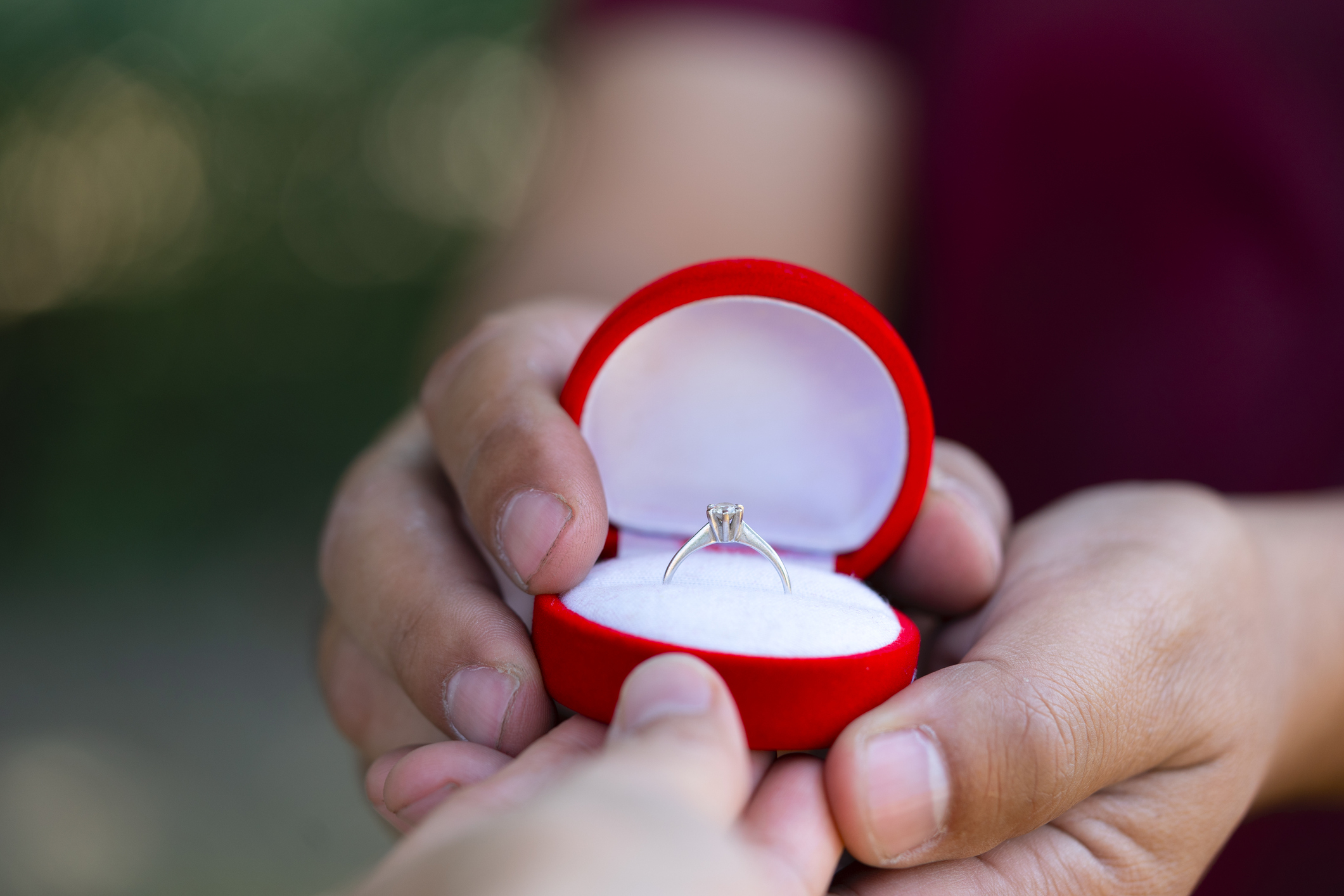 Person holding an engagement ring box open with a ring inside