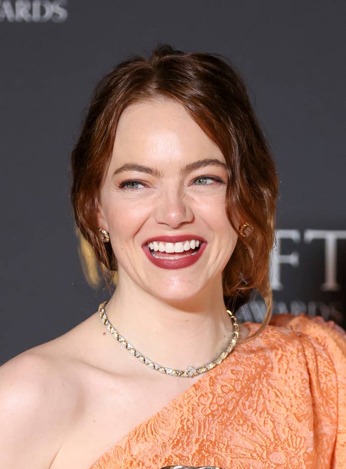 Emma smiling at an event wearing a gemstone necklace and an off-shoulder dress