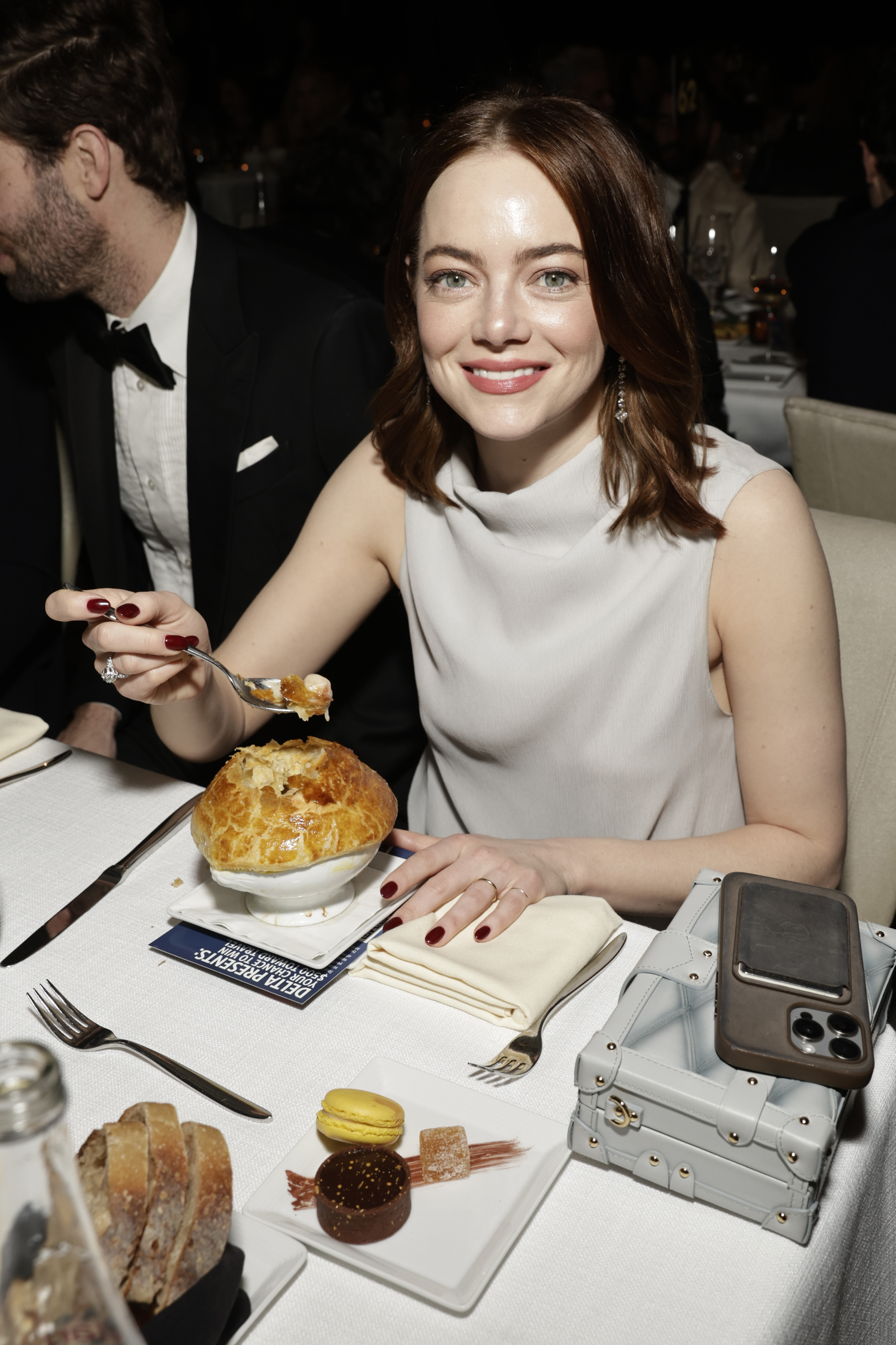 Emma in a sleeveless dress at a table with a pot pie, smiling at the camera