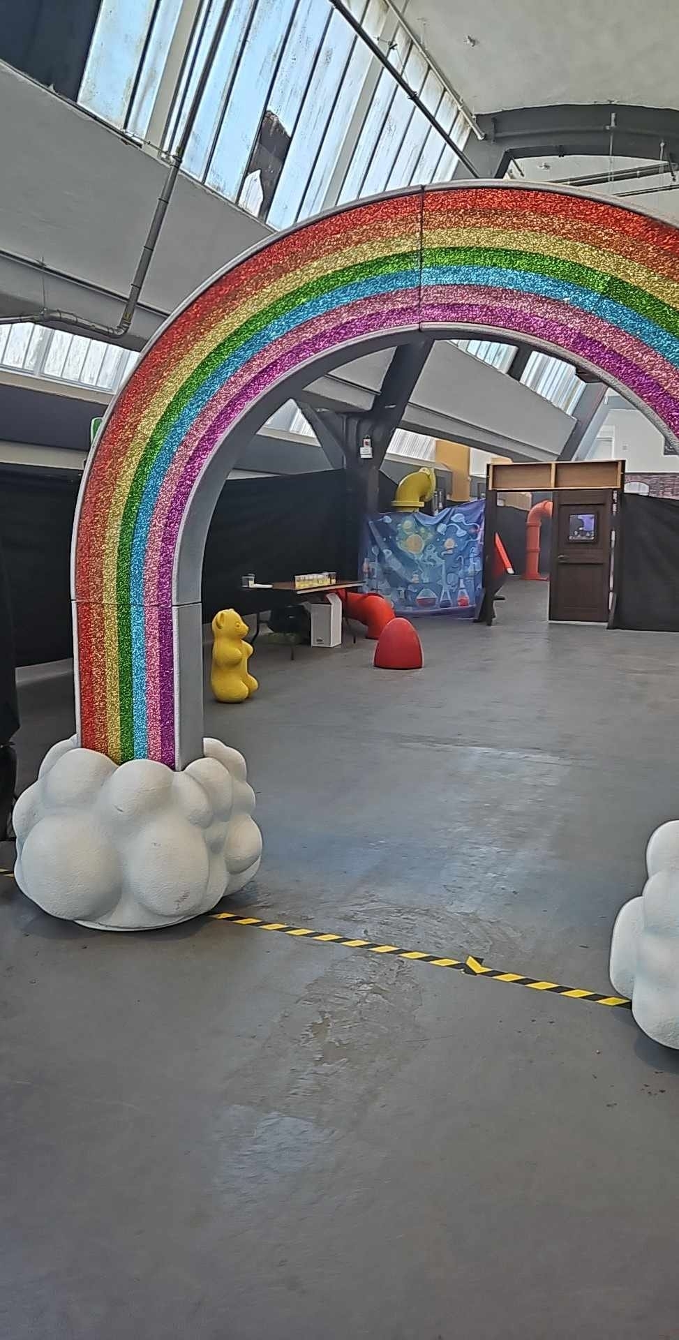 A rainbow arch installation in an indoor industrial space with a small yellow duck sculpture