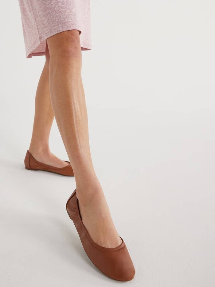 Close-up of a person&#x27;s lower legs wearing flat brown shoes, dressed in a pink skirt