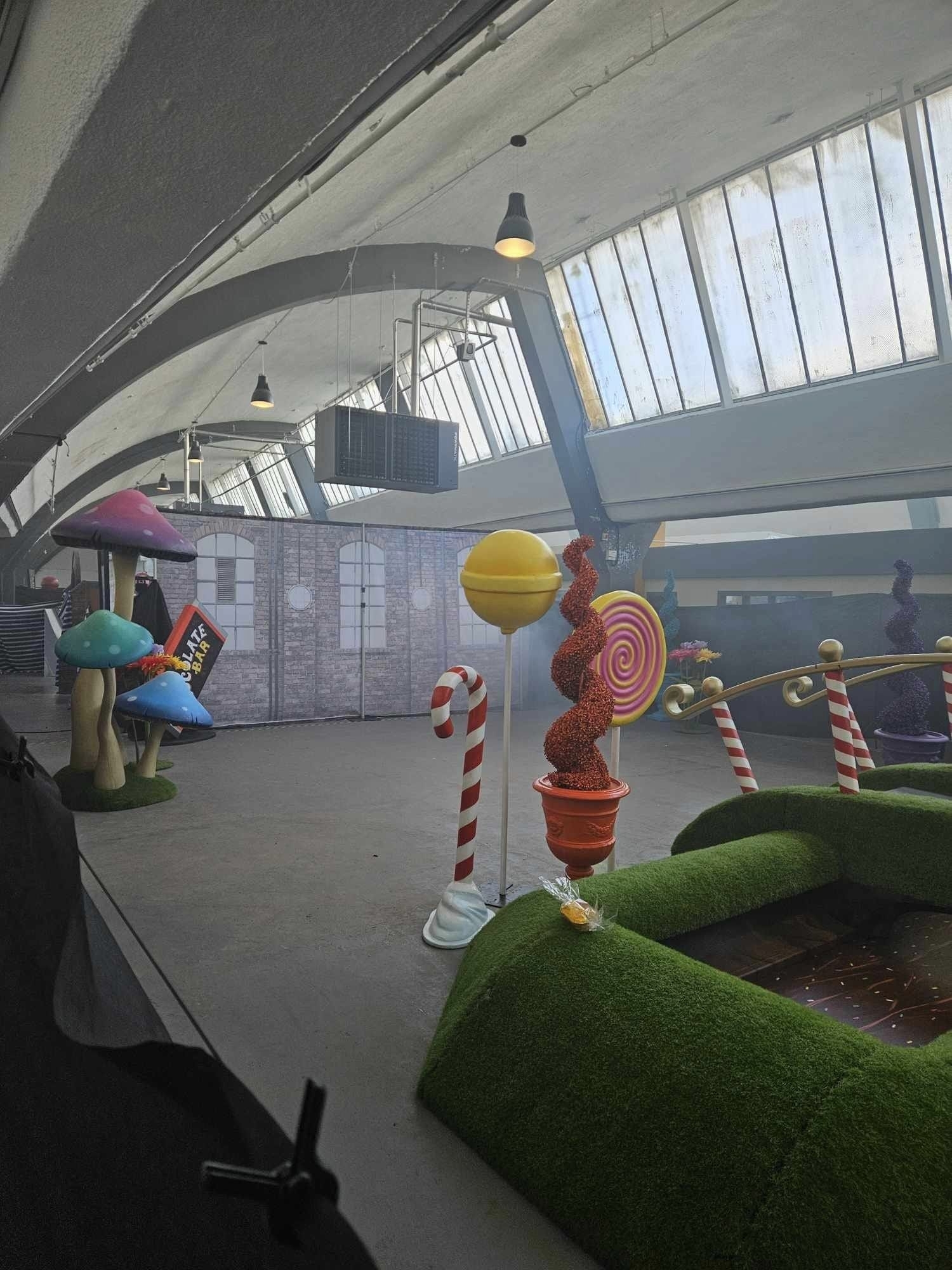 Indoor candy-themed area with oversize candy decorations and artificial turf and a fake brick wall that you can see over