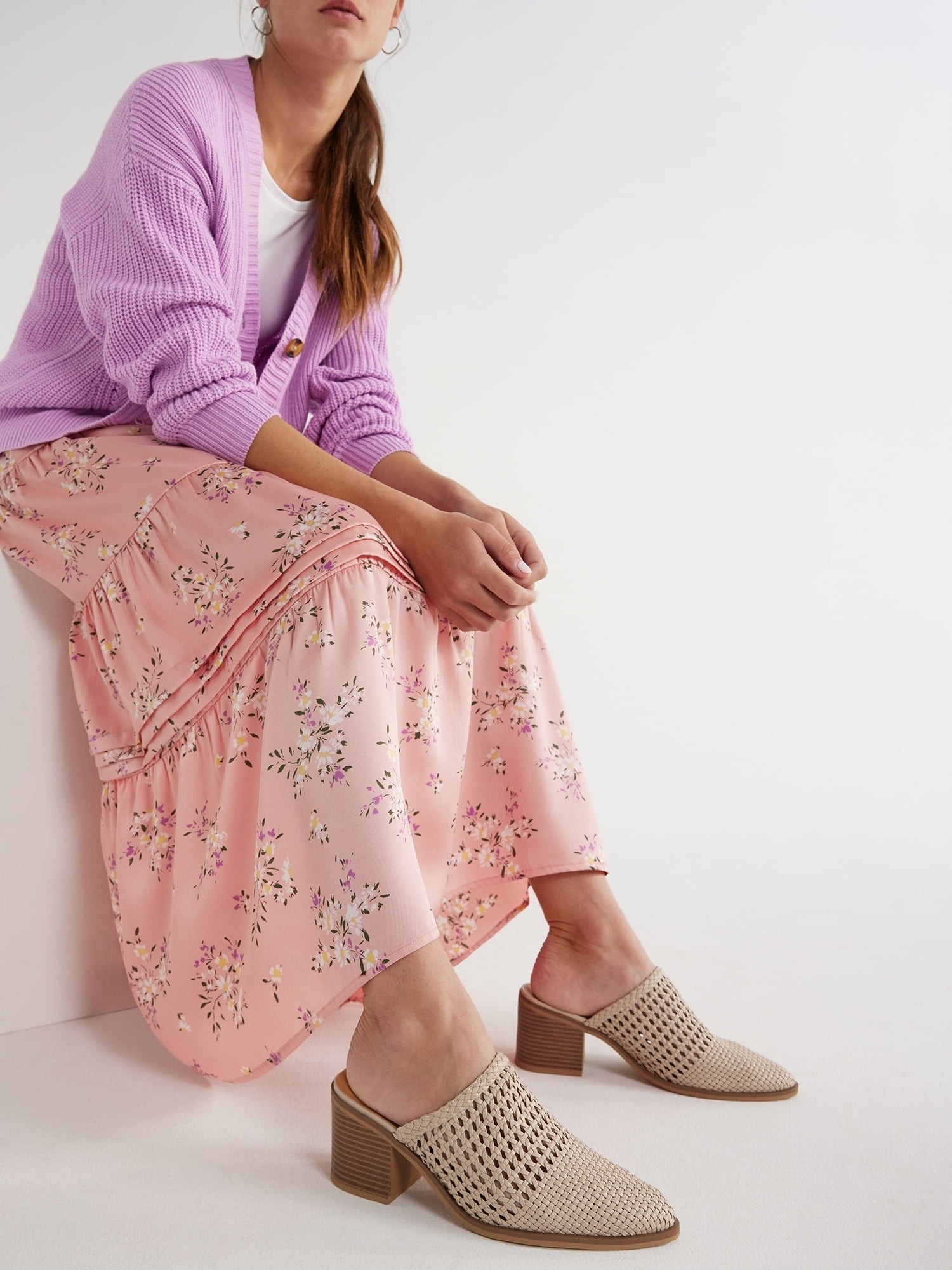 Person seated wearing a lavender cardigan, floral skirt and tan woven heeled shoes