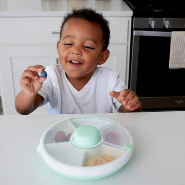 Child smiling at a snack tray with multiple compartments on kitchen counter