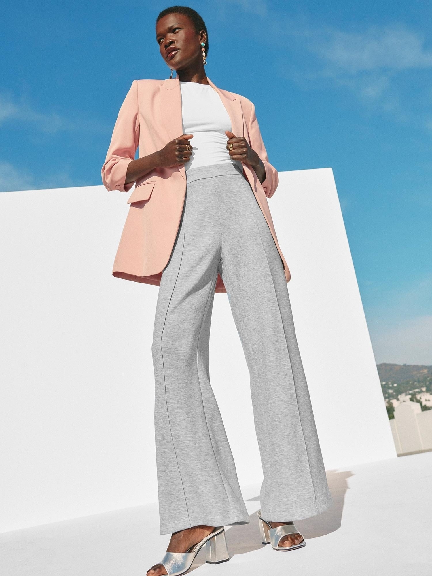 model in a business casual attire with a blazer, wide-leg trousers, and silver heeled sandals, standing against a white backdrop