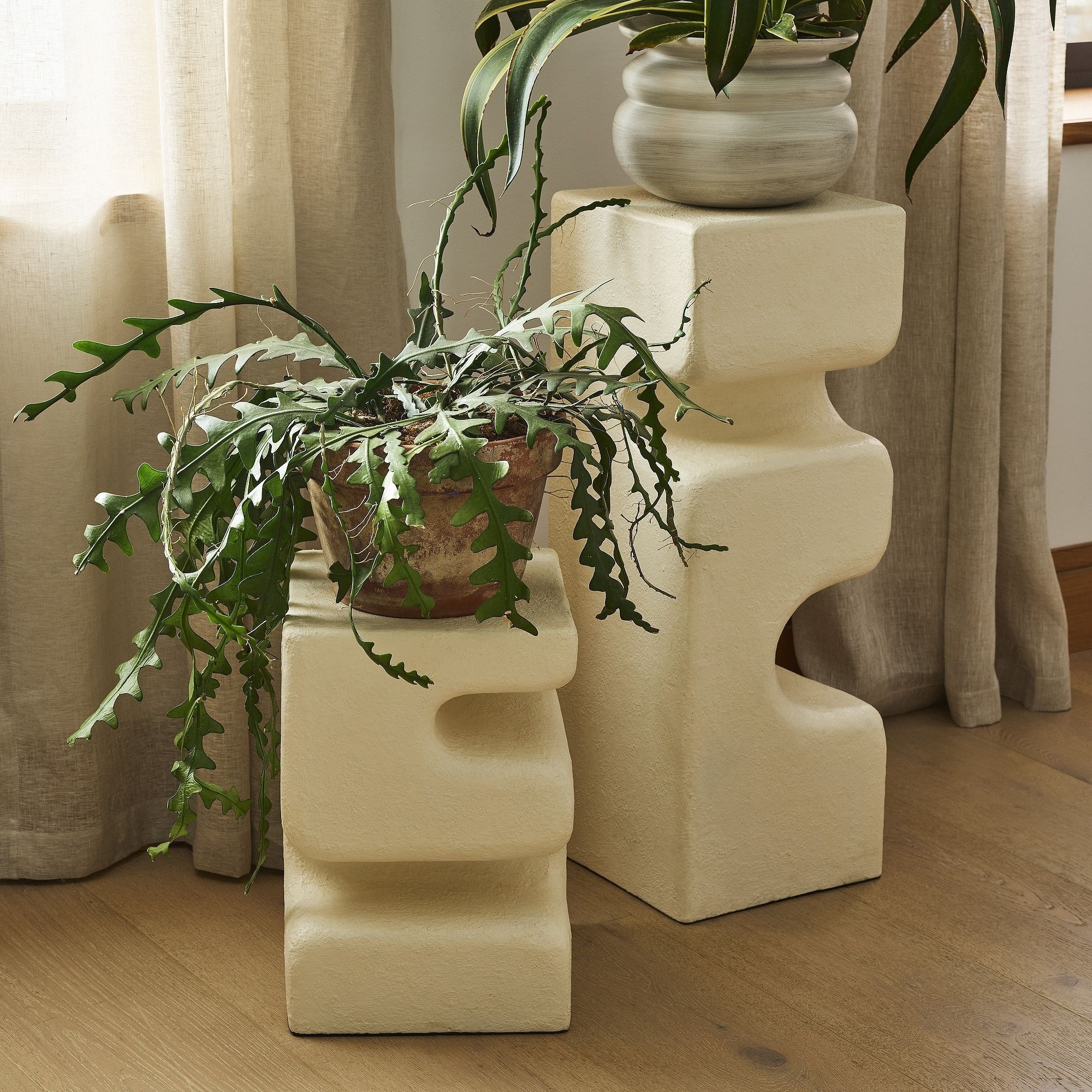 Two unique sculptural bookends holding a potted plant on a wooden floor, ideal for stylish interior decor